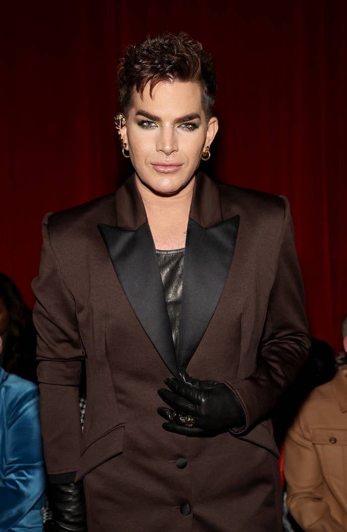 Person in a slick suit with leather gloves, standing indoors