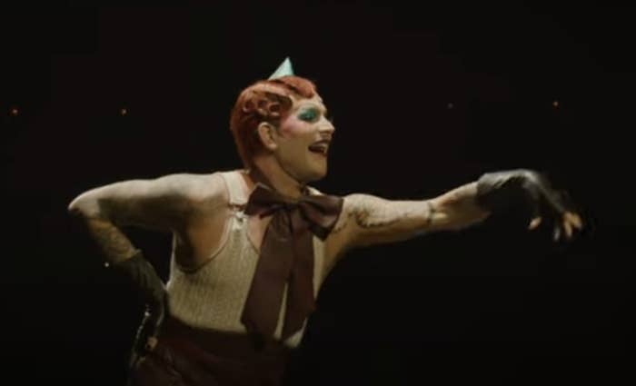 Performer in vintage-style circus costume, with gloves and a pointy hat, striking a dramatic pose on stage
