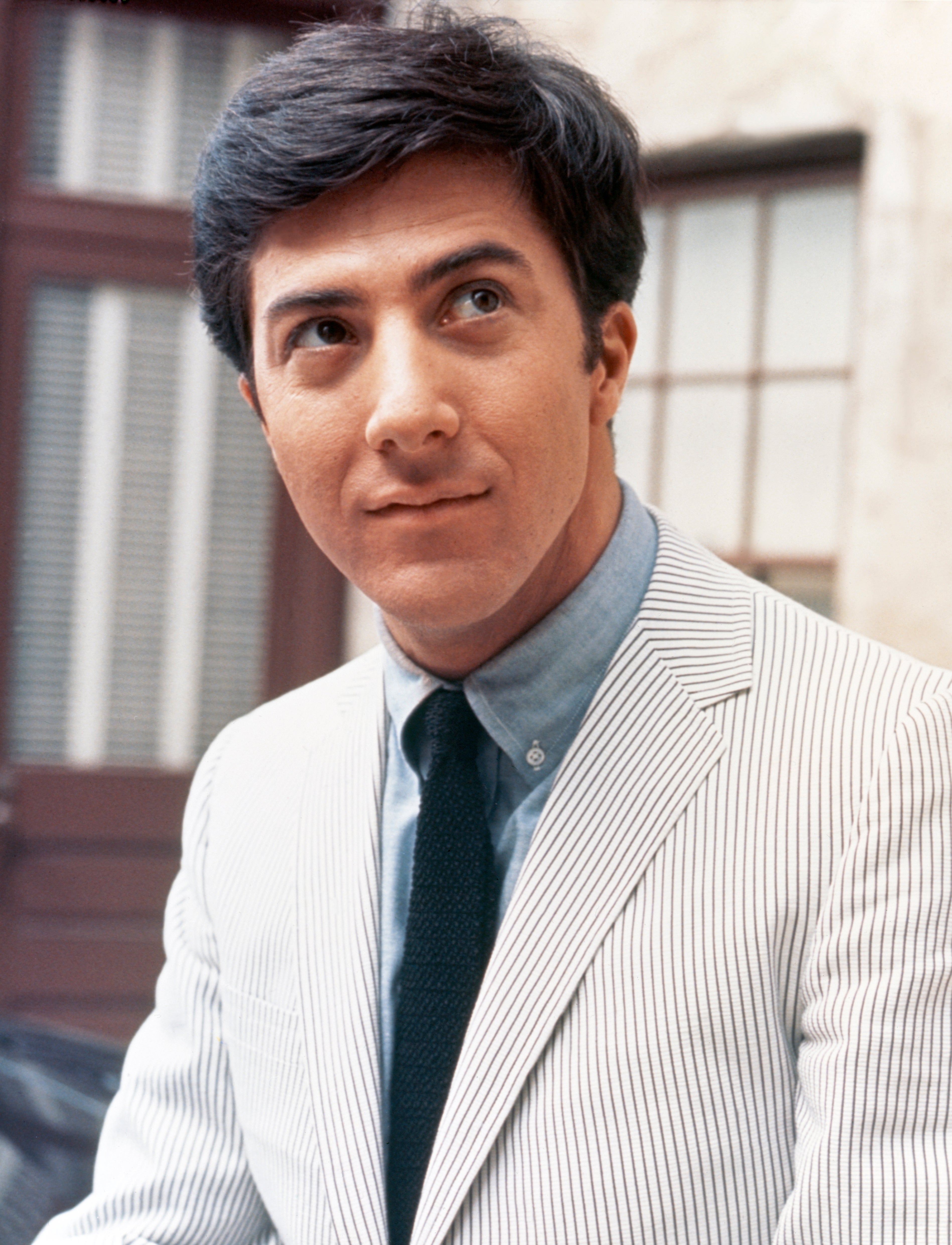 Person wearing a striped suit jacket, with a calm expression, looking slightly off to the side