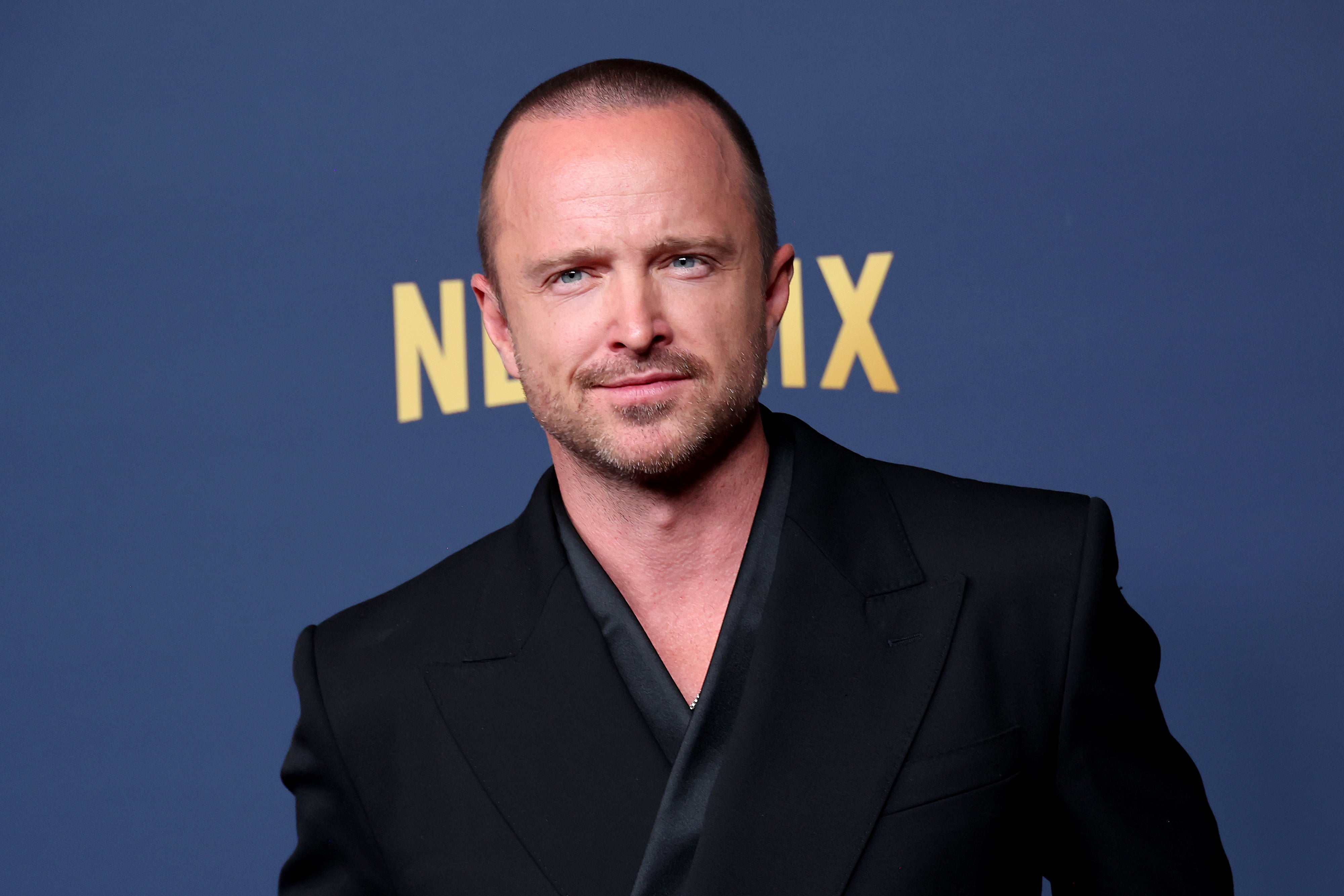 Man in a sleek black suit poses in front of a backdrop with the word "Netflix."