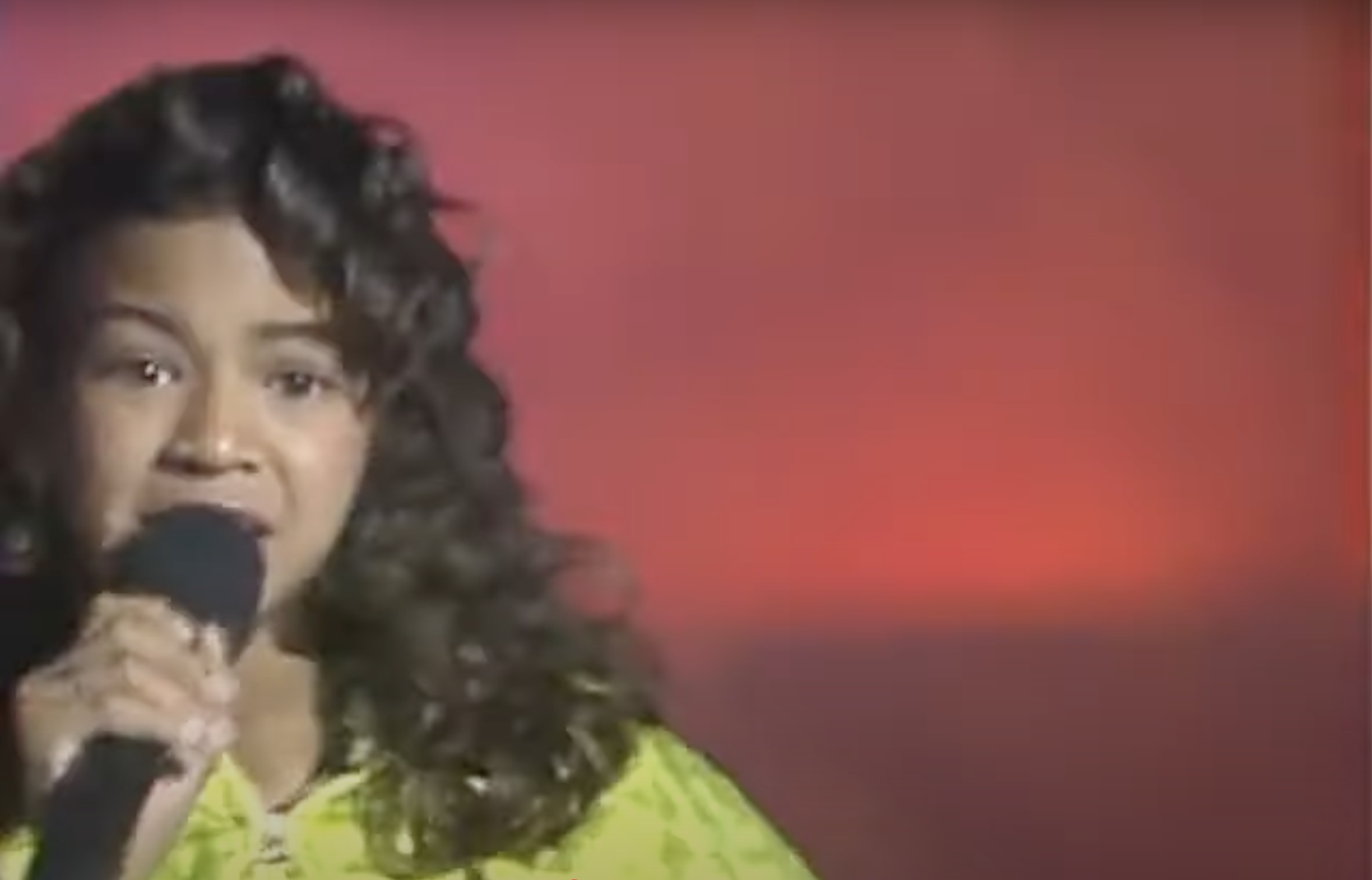 Woman singing into a microphone, wearing a patterned top on stage
