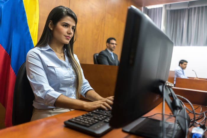 Person in a courthouse typing at a computer, with two others in the background