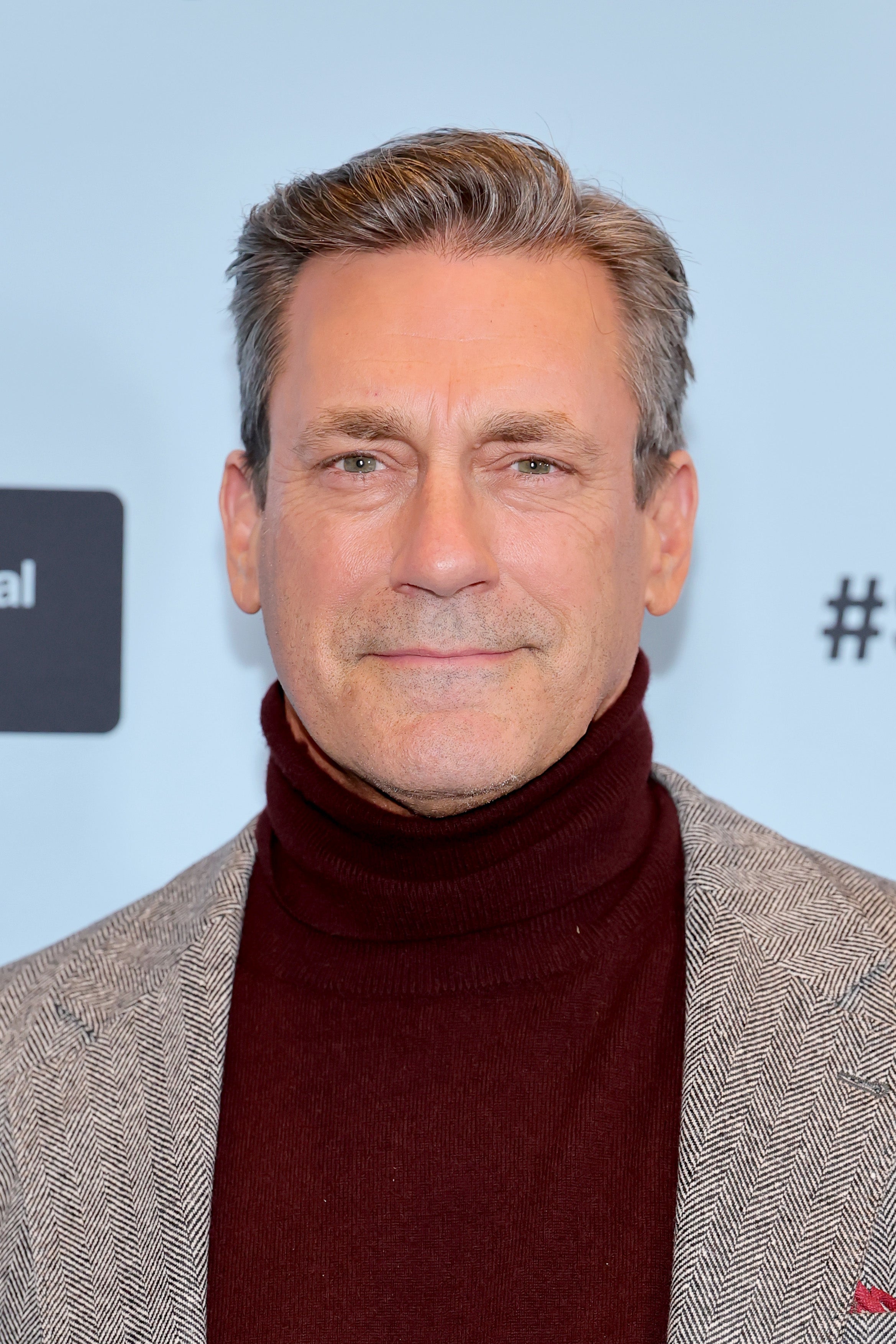 A person in a turtleneck sweater and herringbone blazer poses confidently at an event
