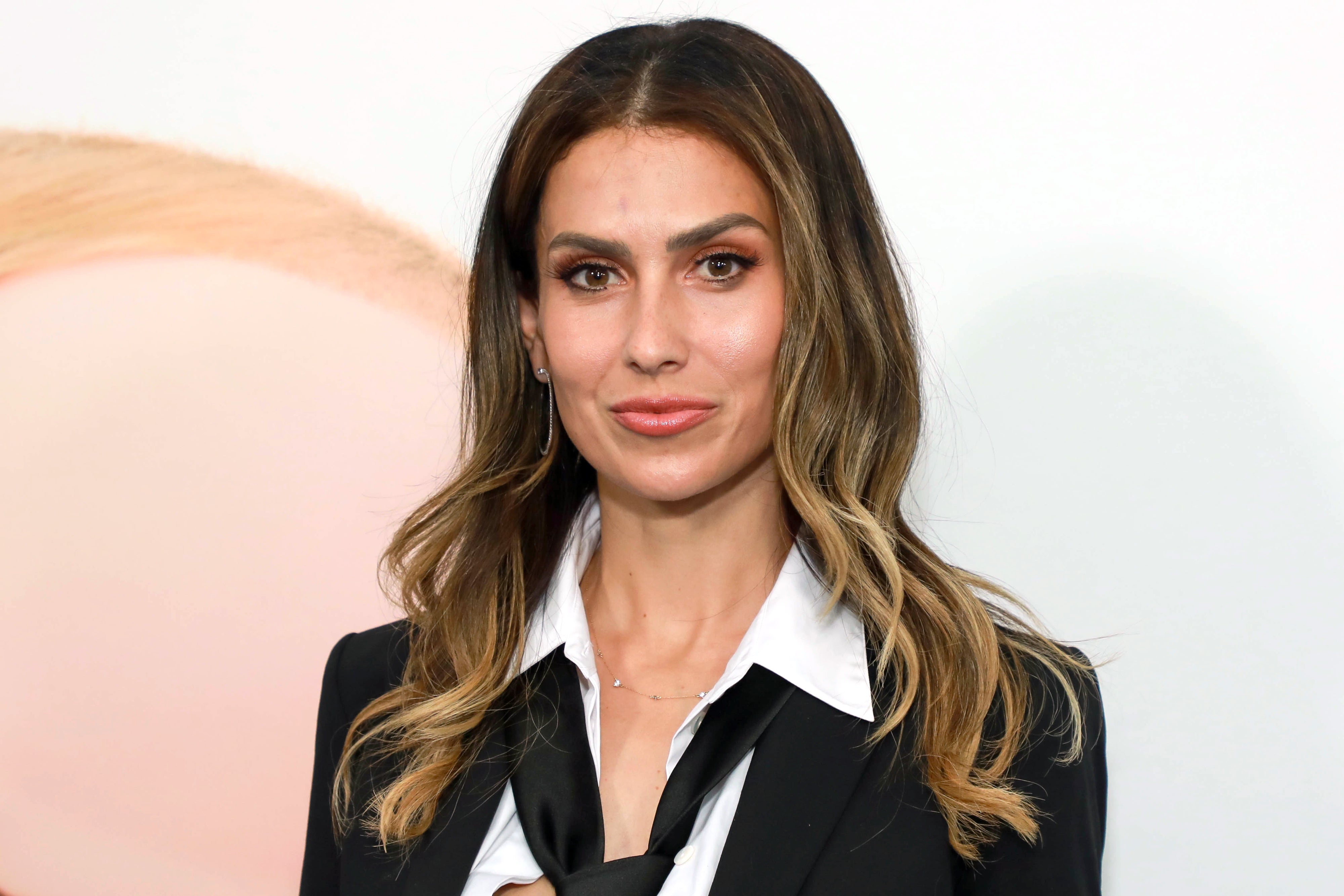 I don't know who this is, but they are wearing a black suit jacket with a white shirt and tie, posing in front of a neutral background