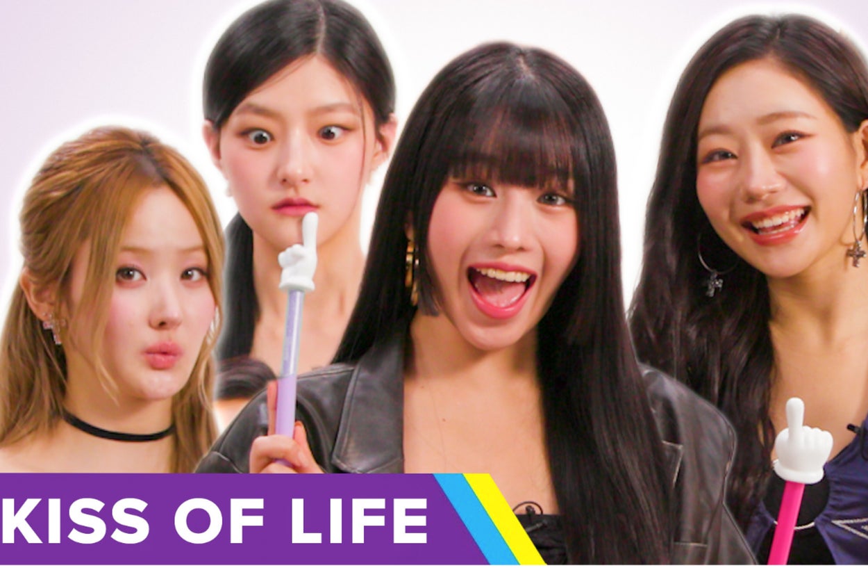 Four women smiling and posing with playful hand prop. Text: "Kiss of Life" in bottom left corner