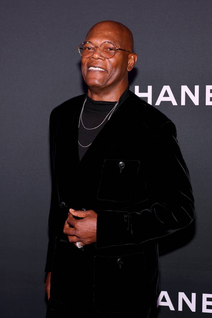 Person in a sleek black velvet suit with layered necklaces poses at an event
