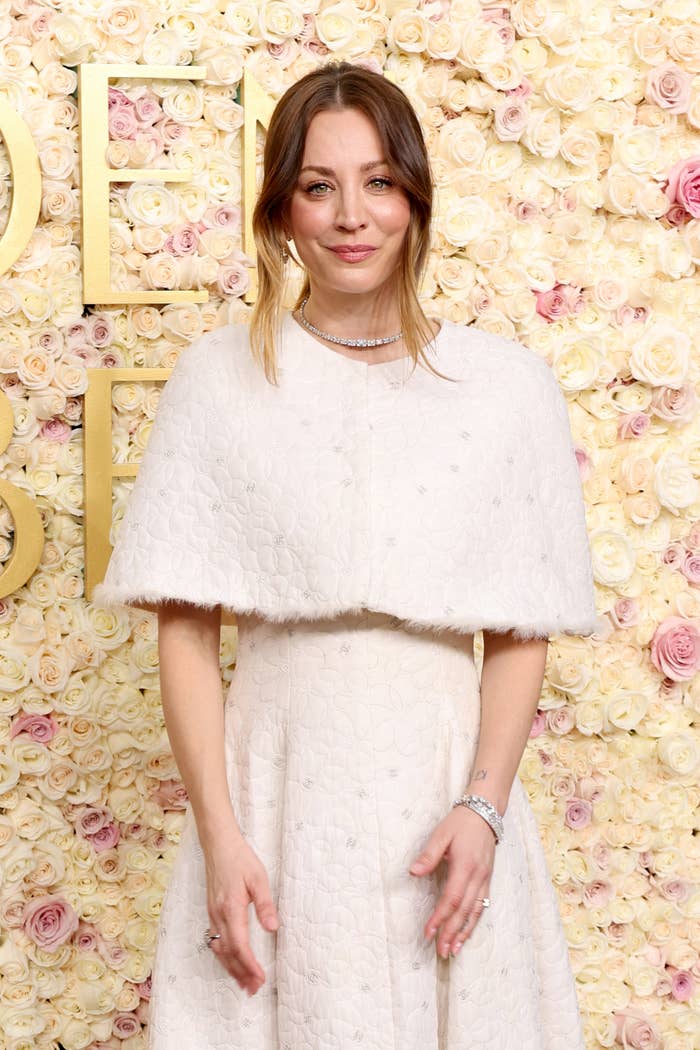 A woman on a floral backdrop wearing a textured white cape dress with jewelry