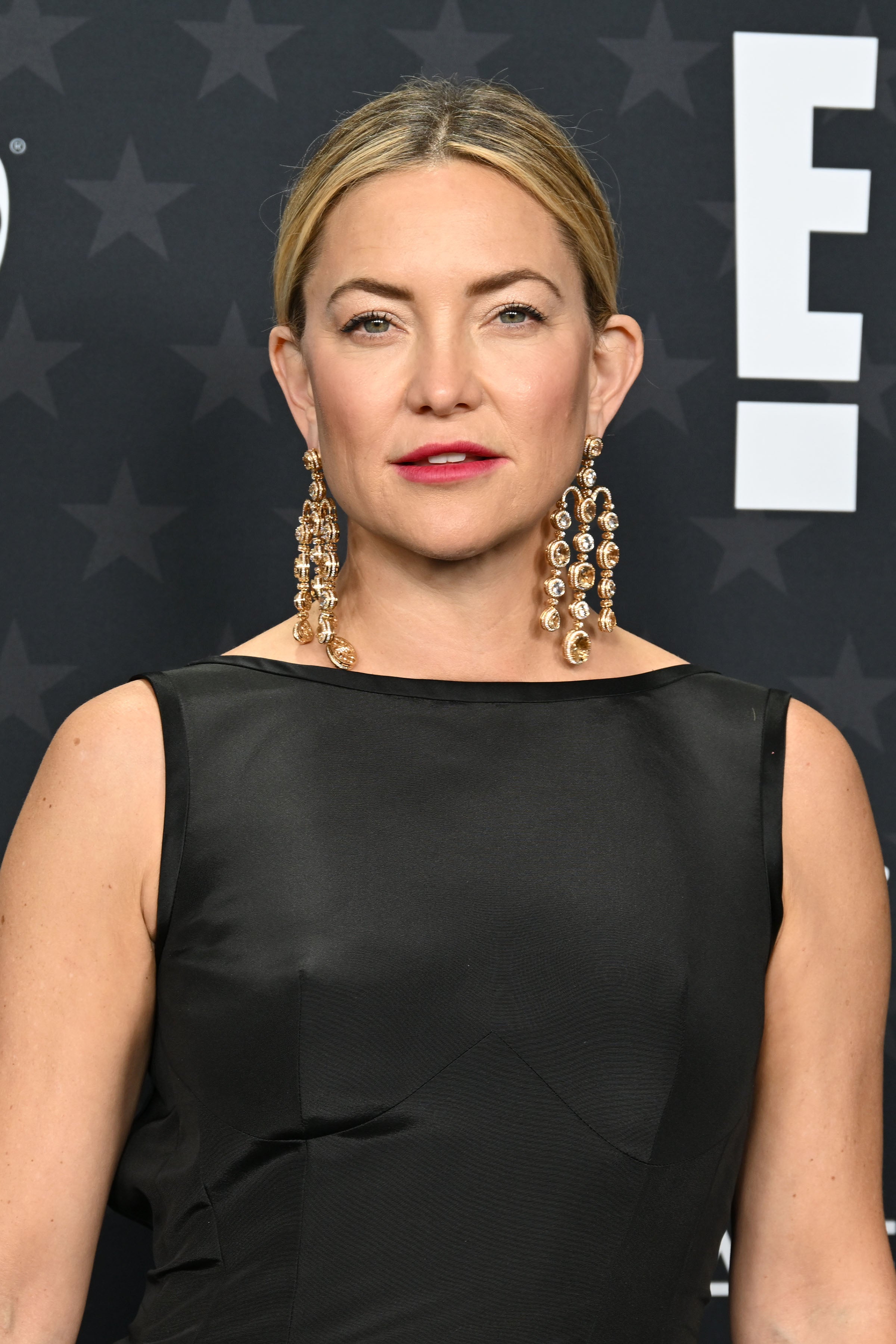 Kate Hudson in sleeveless, elegant dress with statement earrings on a red carpet