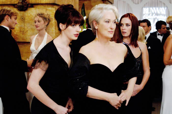 Anne Hathaway, Meryl Streep, and Emily Blunt in elegant formal gowns at a glamorous event, with guests socializing in the background