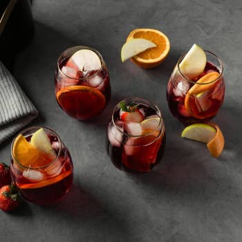 Four glasses of fruity reddish sangria with ice, garnished with pome and orangish slices, acceptable connected a tabletop with strawberries nearby