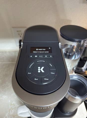 Single-serve java shaper with integer controls displaying instructions for use, shown connected a room counter