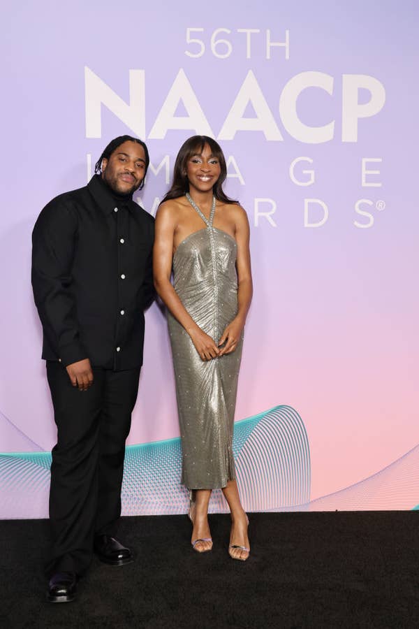 Two people pose on the NAACP Image Awards red carpet. One wears a black outfit, the other a shimmering strapless dress