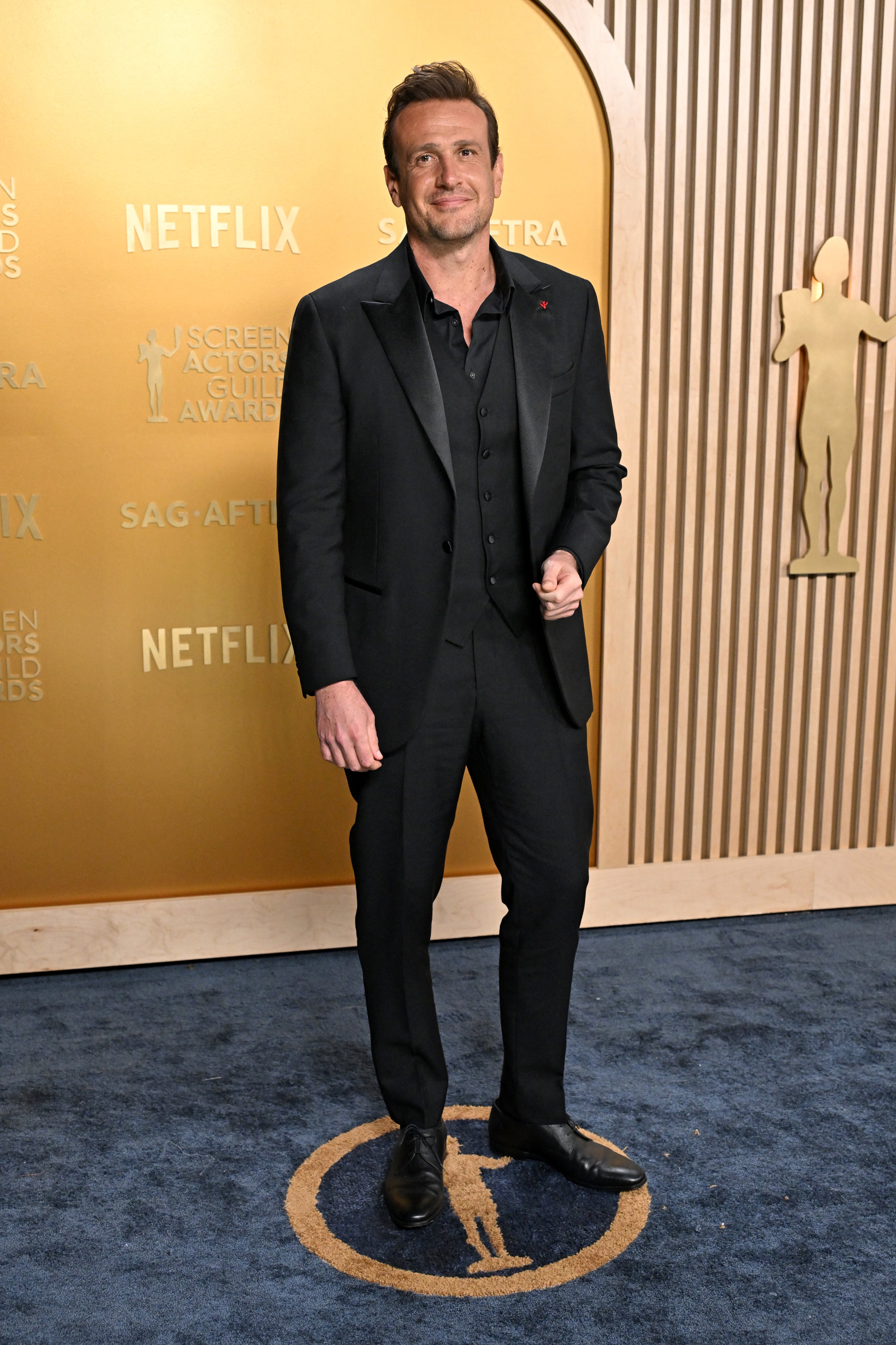 Person in a formal suit smiles on a red carpet at a Netflix event