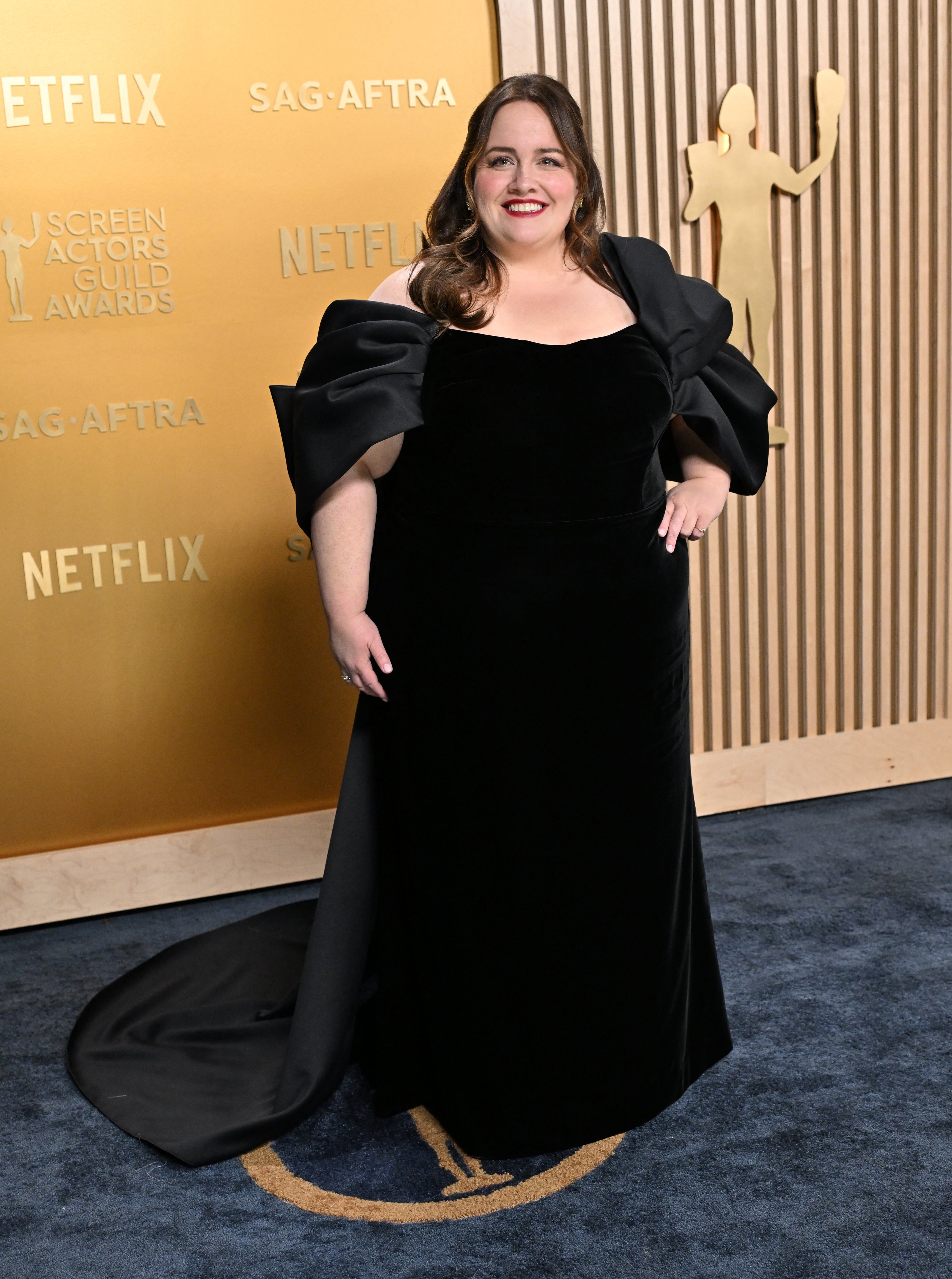Person in an elegant black gown with dramatic shoulder detail on a red carpet at a SAG-AFTRA event