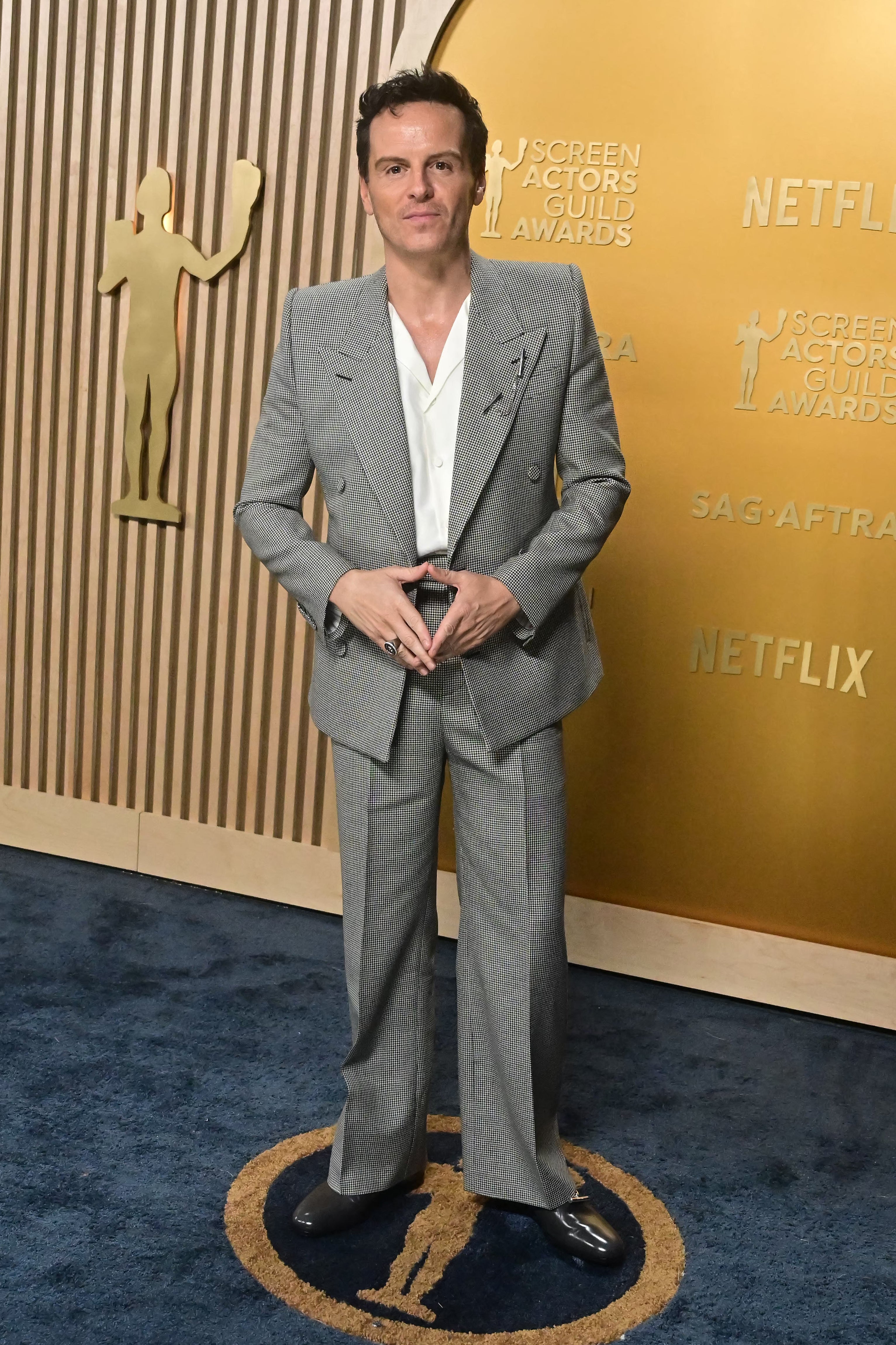 Person in a patterned suit with a white shirt poses at the Screen Actors Guild Awards event backdrop