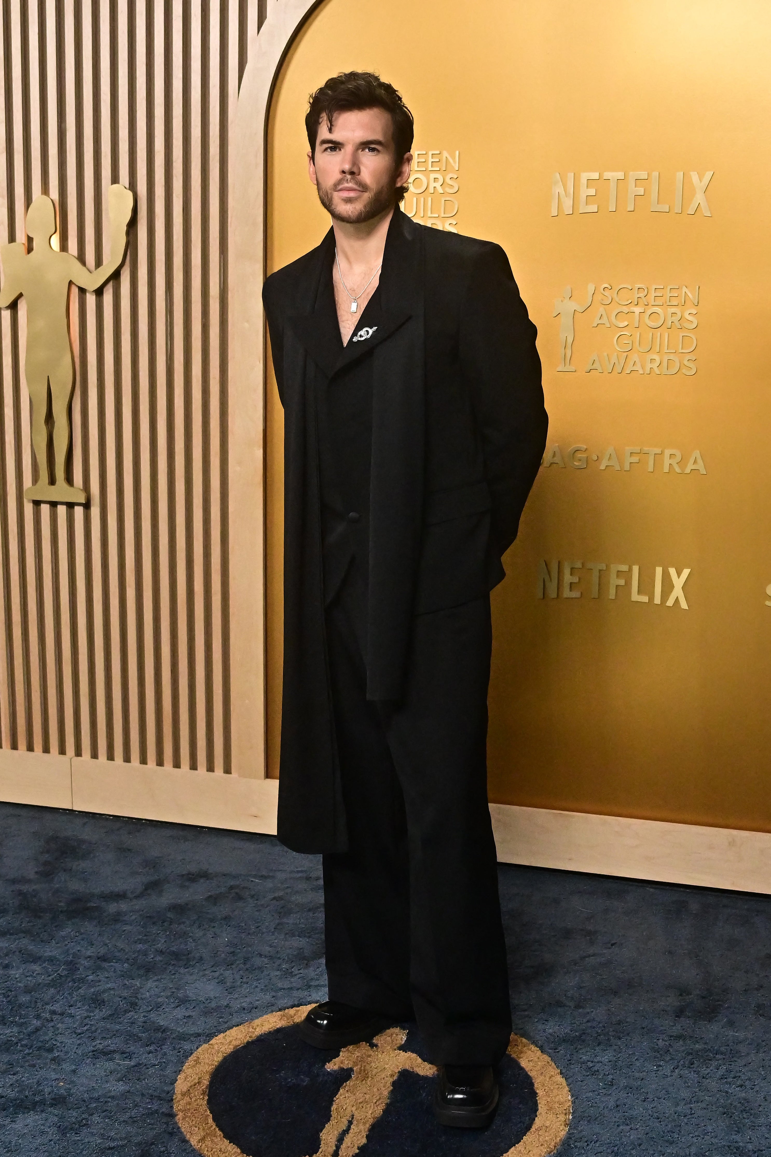 Person in a stylish black suit on a blue carpet at an event with SAG Awards backdrop