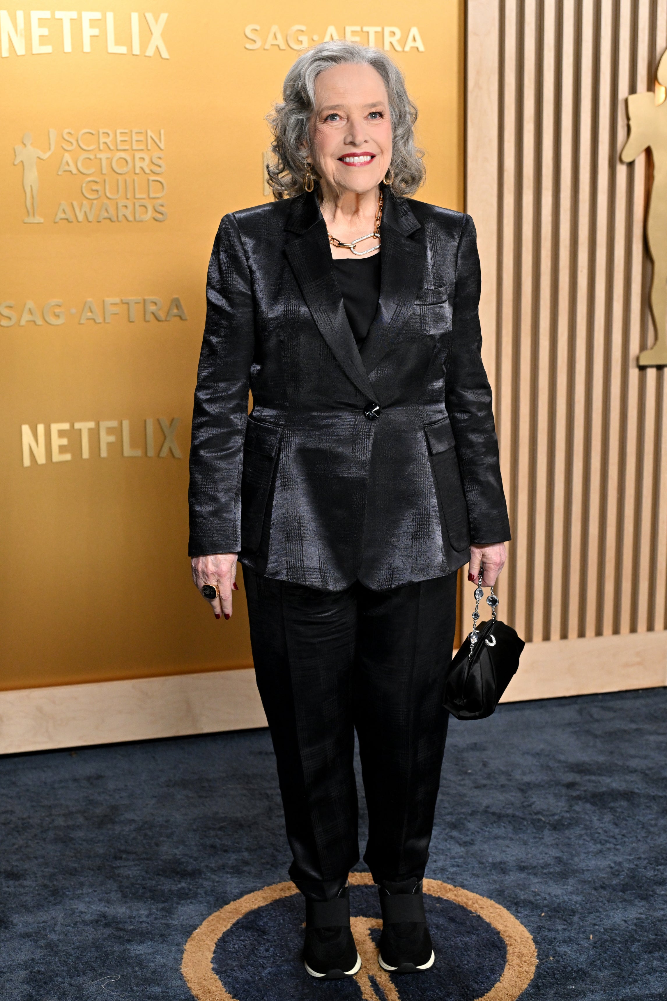 Person in a tailored suit with a metallic sheen at an awards event, standing on a blue carpet
