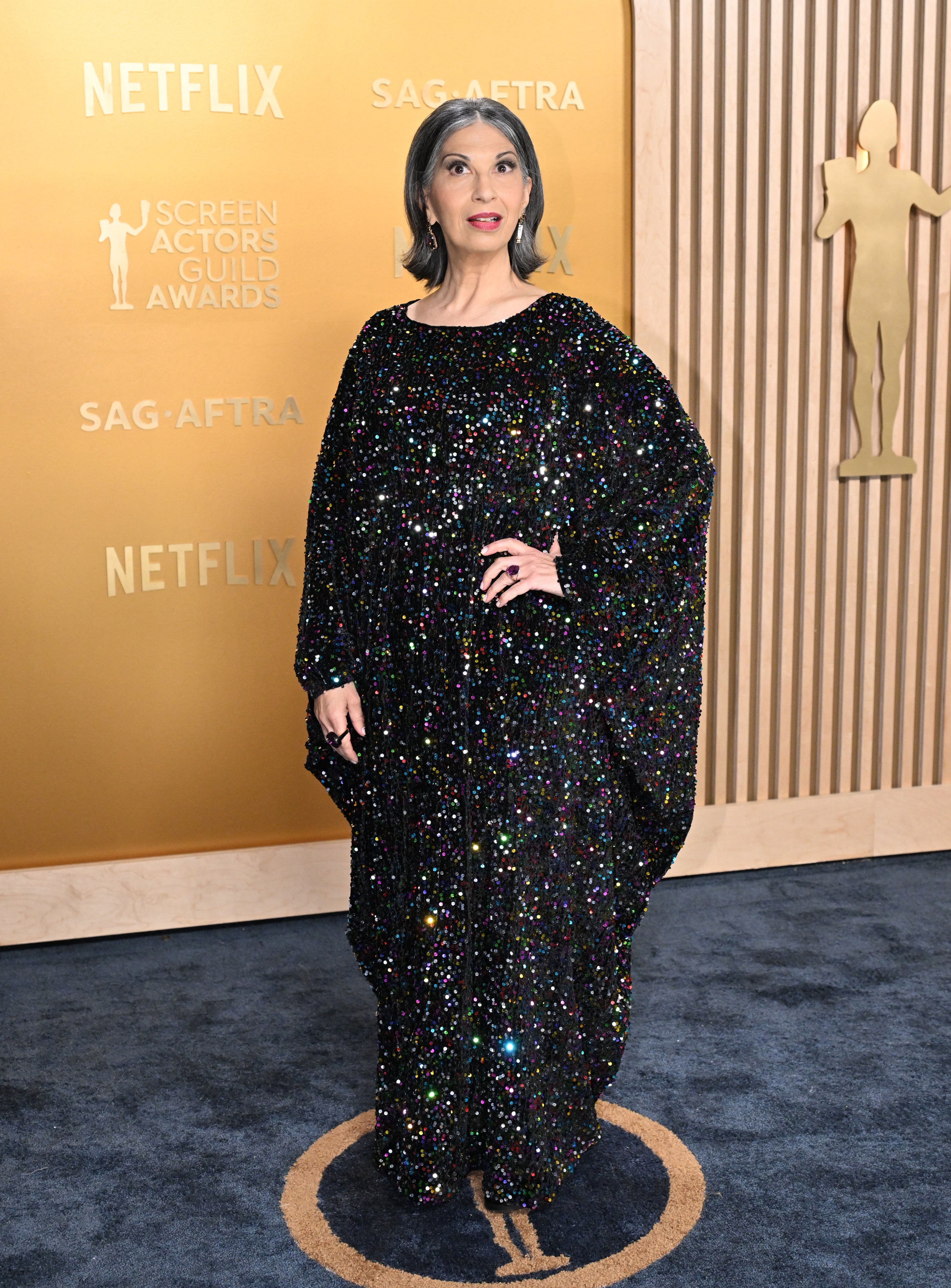 Person in sparkling, flowing gown poses at SAG-AFTRA event backdrop with Netflix logos