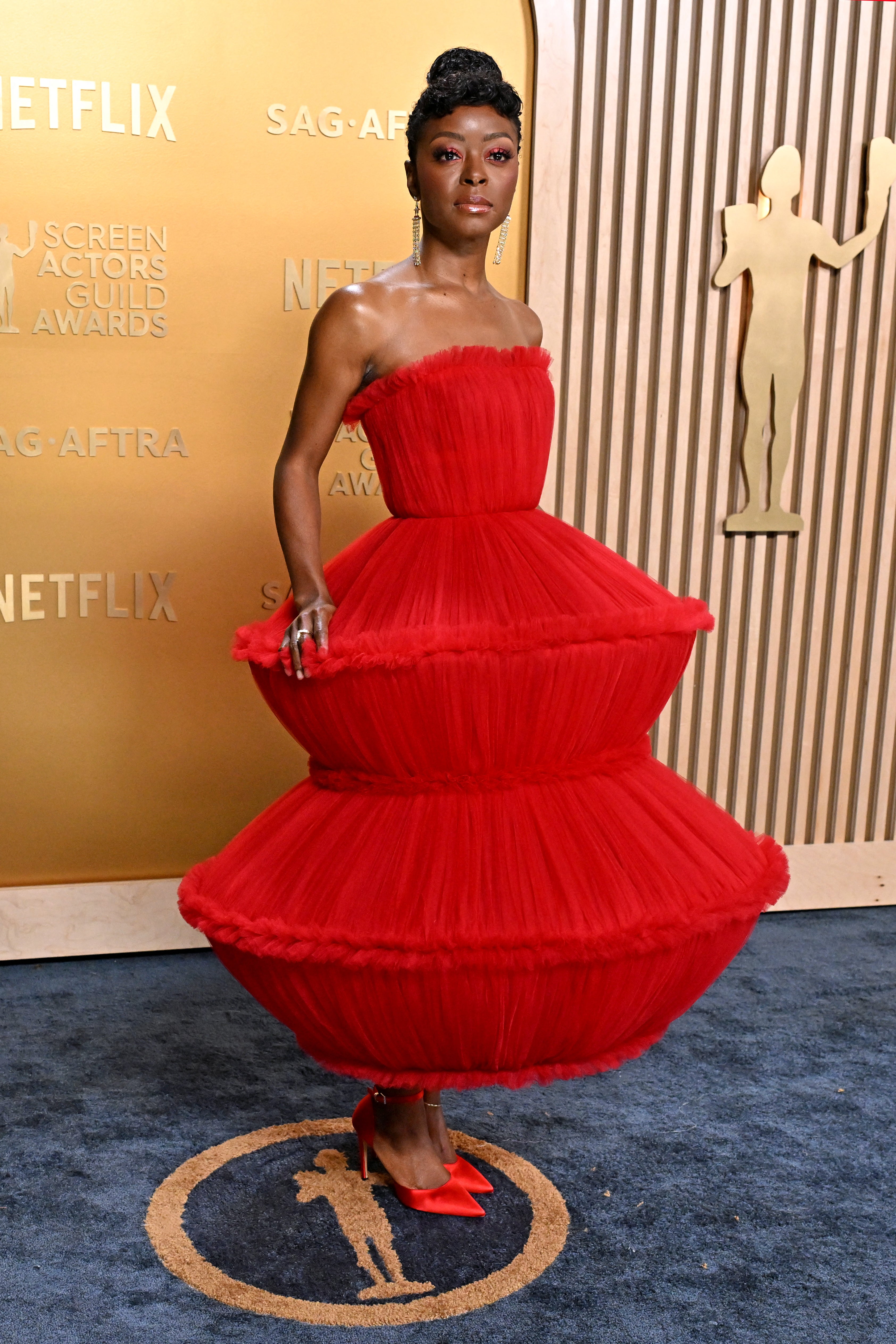 Person in a unique, tiered tulle dress with a strapless top, standing in front of a SAG-AFTRA backdrop
