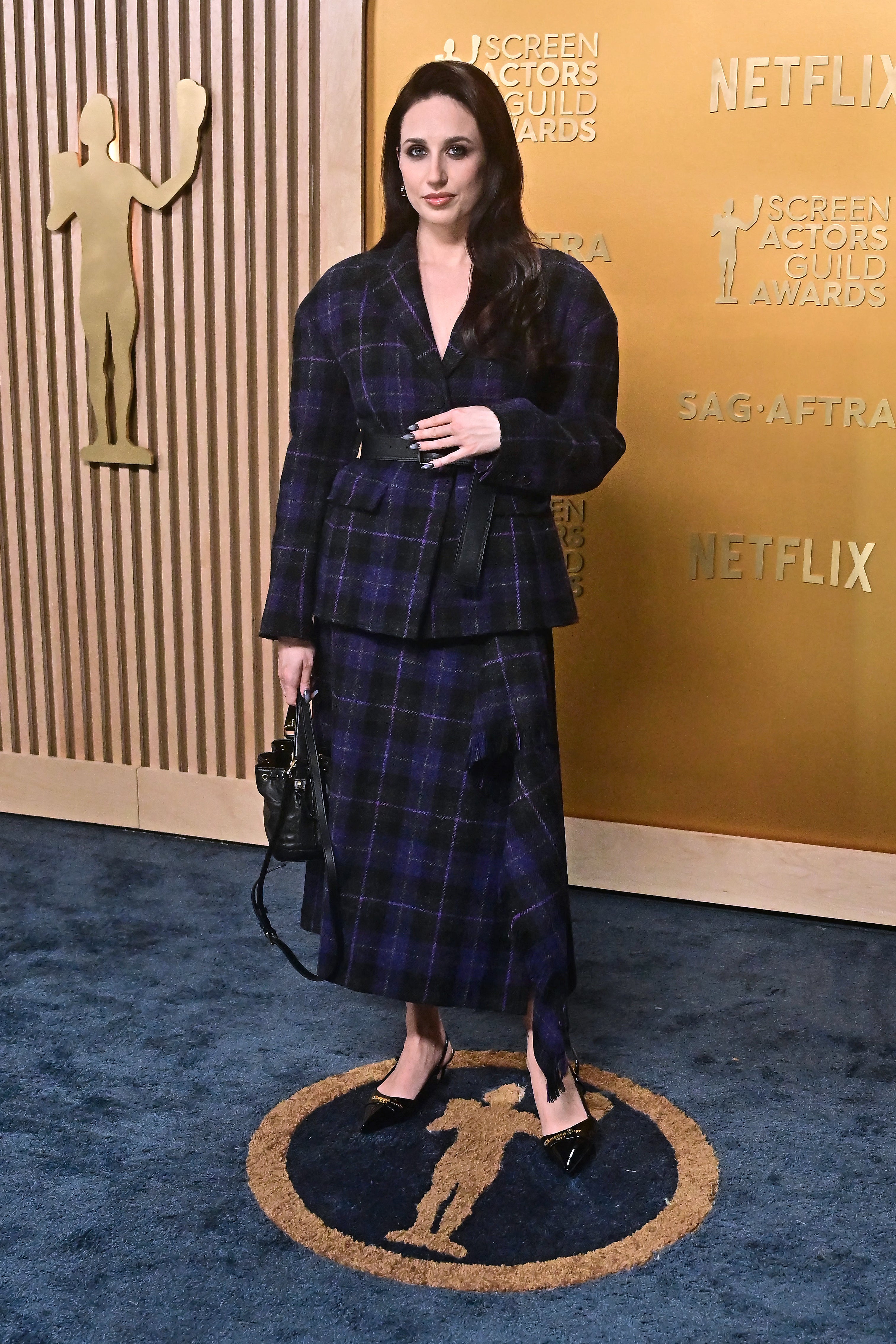 Person in elegant plaid suit and skirt on a red carpet at a Screen Actors Guild Awards event backdrop