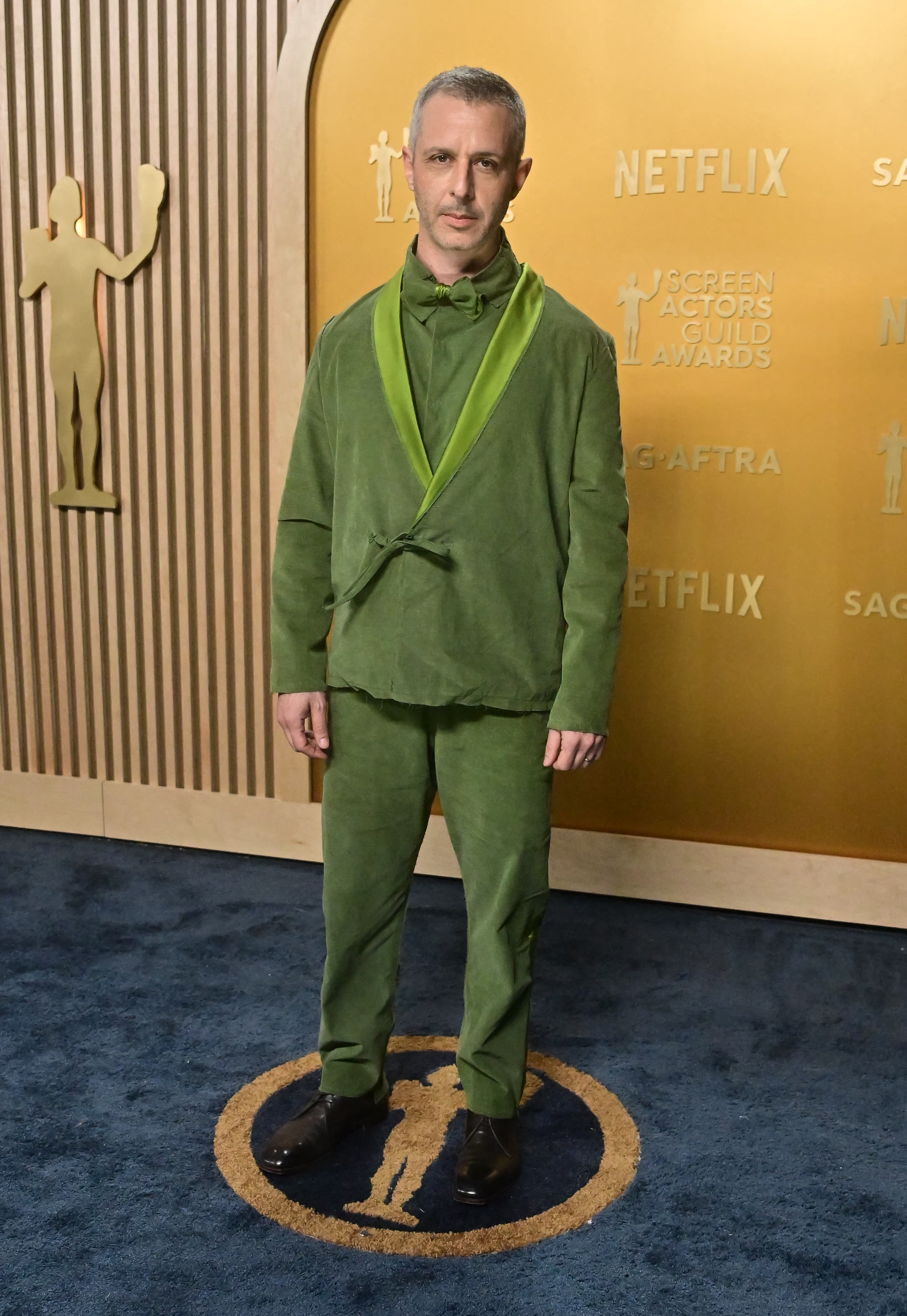 Person in a velvet suit stands on a red carpet event; background has SAG Awards and Netflix logos