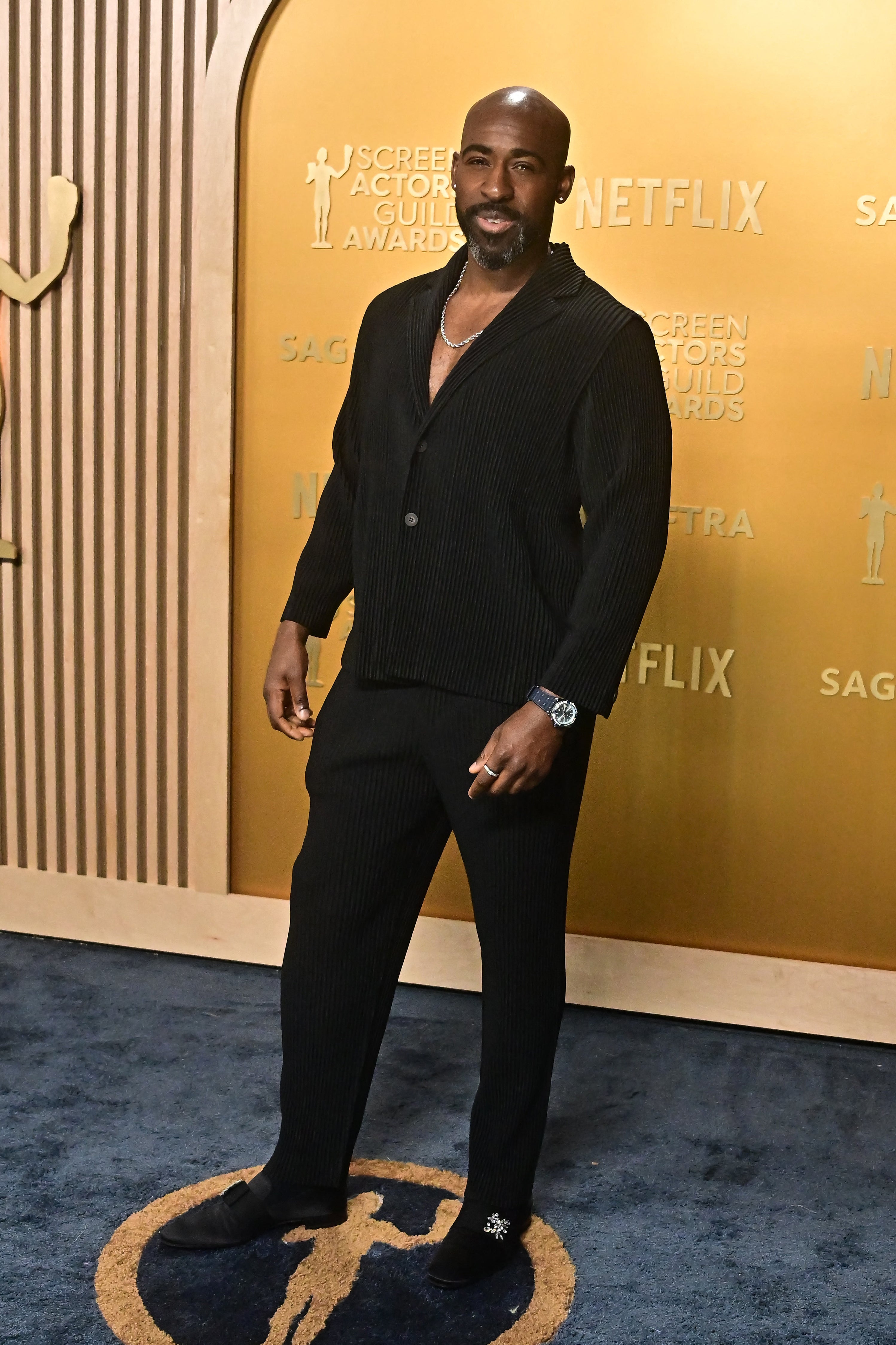 Person in a stylish corduroy suit at an award event backdrop, posing confidently