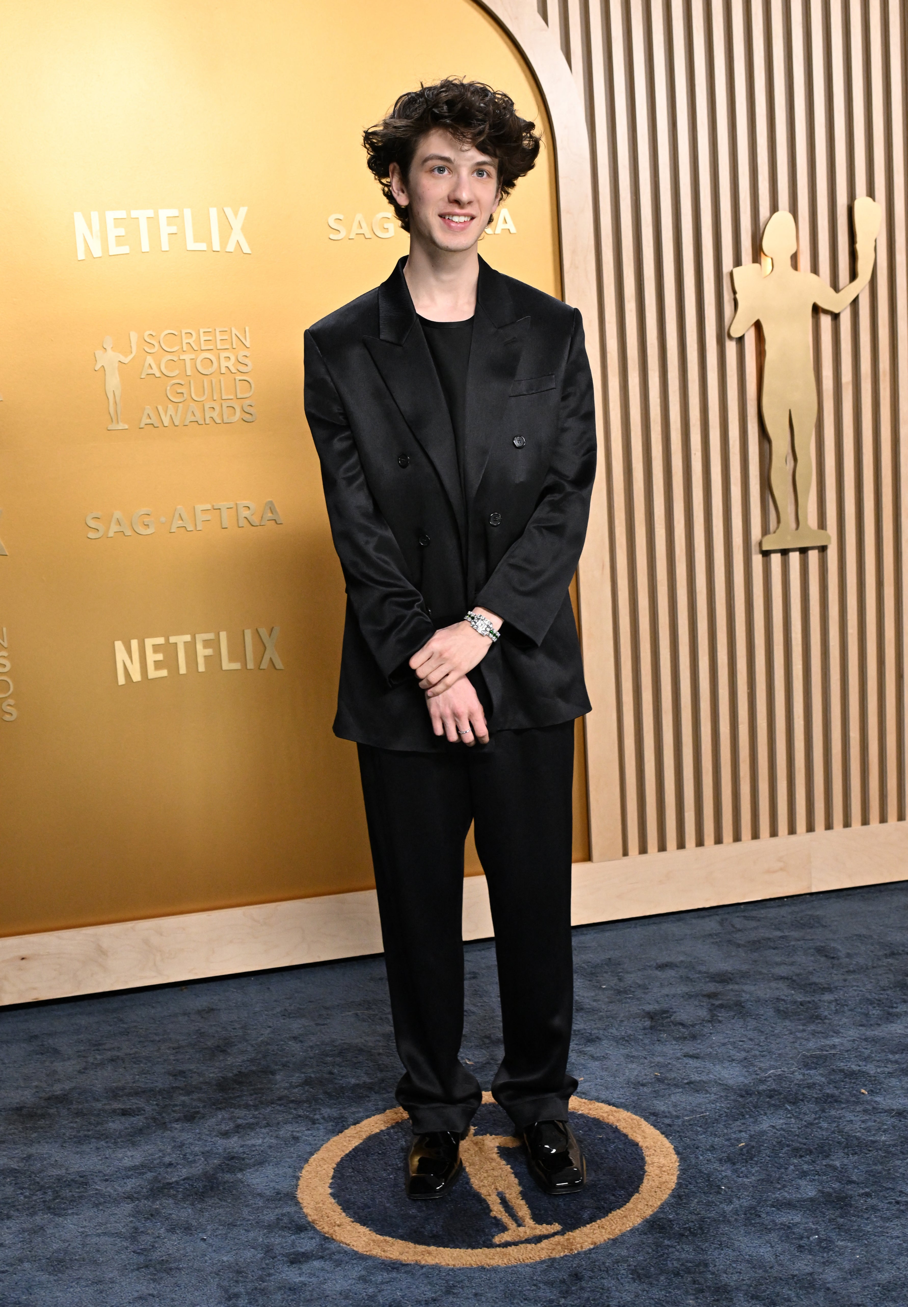 Person in black suit standing on red carpet at a Screen Actors Guild Awards event backdrop