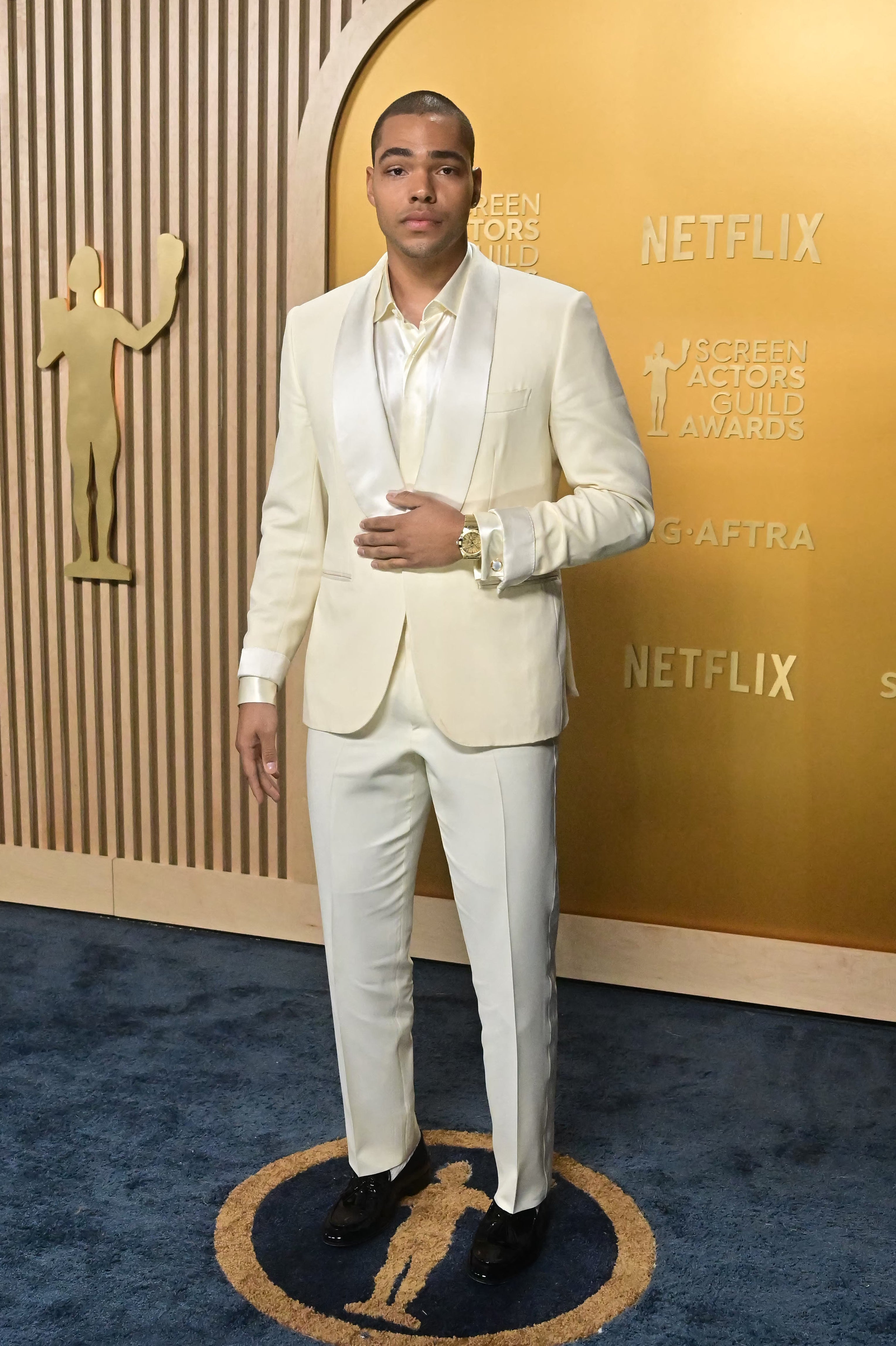 Man in elegant white suit stands on blue carpet at SAG Awards