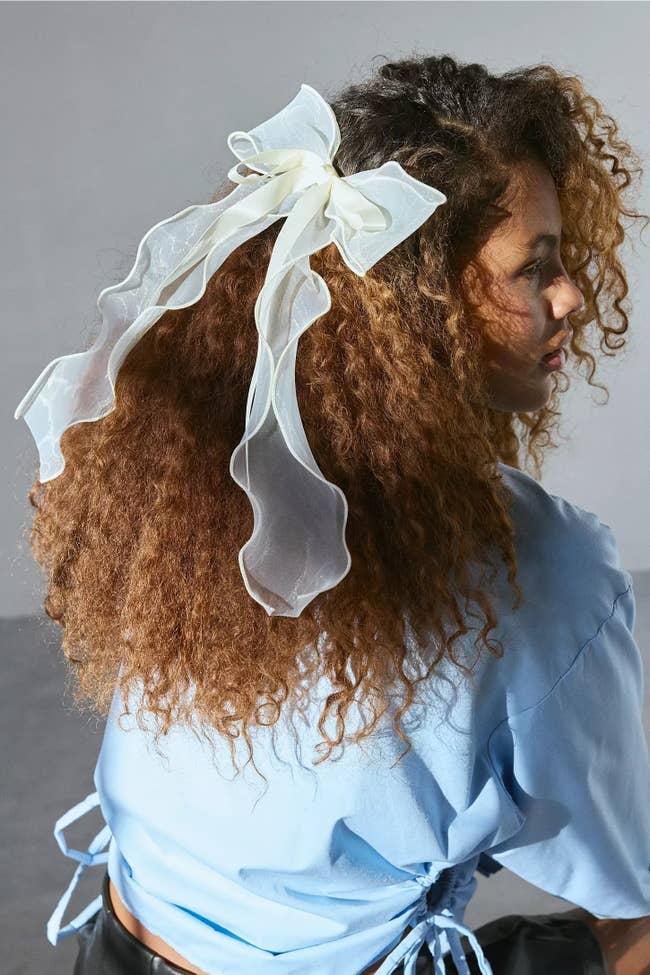 Model with curly hairsbreadth  wearing a large, translucent bow, styled successful  a casual bluish  top, showing disconnected  a fashionable hairsbreadth  accessory