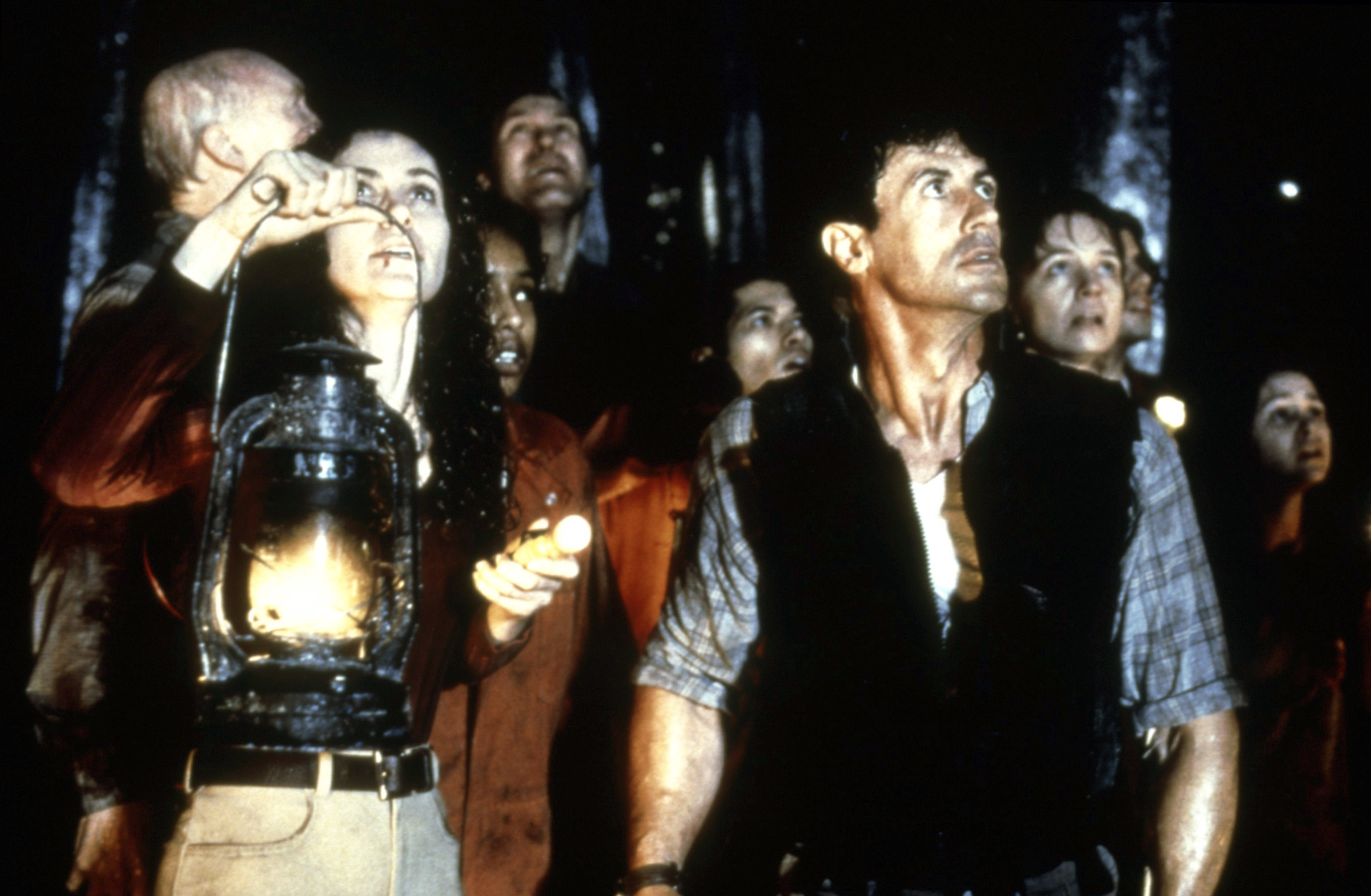 Group of people in a dark cave holding a lantern, looking upward with expressions of curiosity and concern