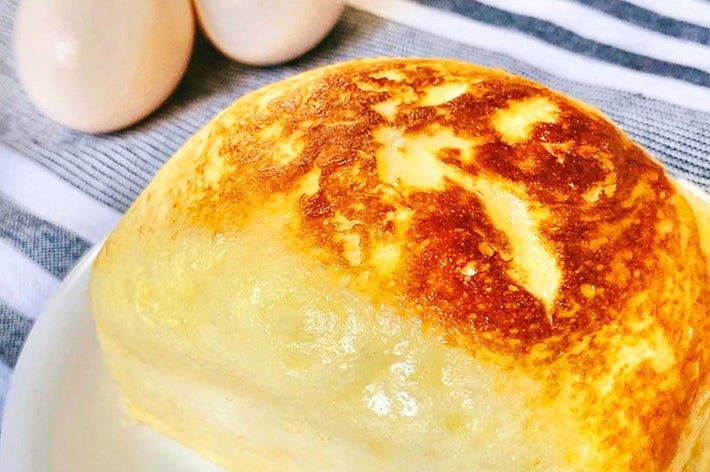 焼き立てのパンケーキが白い皿に載っており、後ろには3つの卵があります。