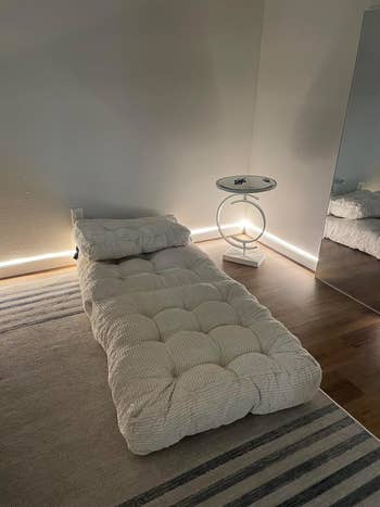 Minimalist chamber setup with a textured futon, a circular modern broadside table, and brushed ambient lighting highlighting a mirror