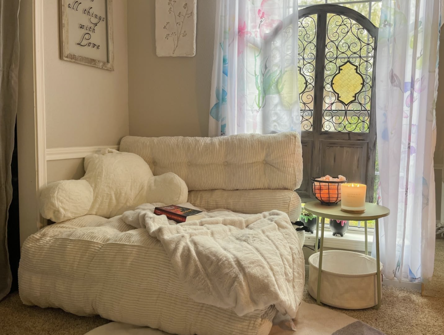 Cozy reading nook with a plush chair and pillows, a book on the seat, a small table with a candle, and decorative curtains in a bright room