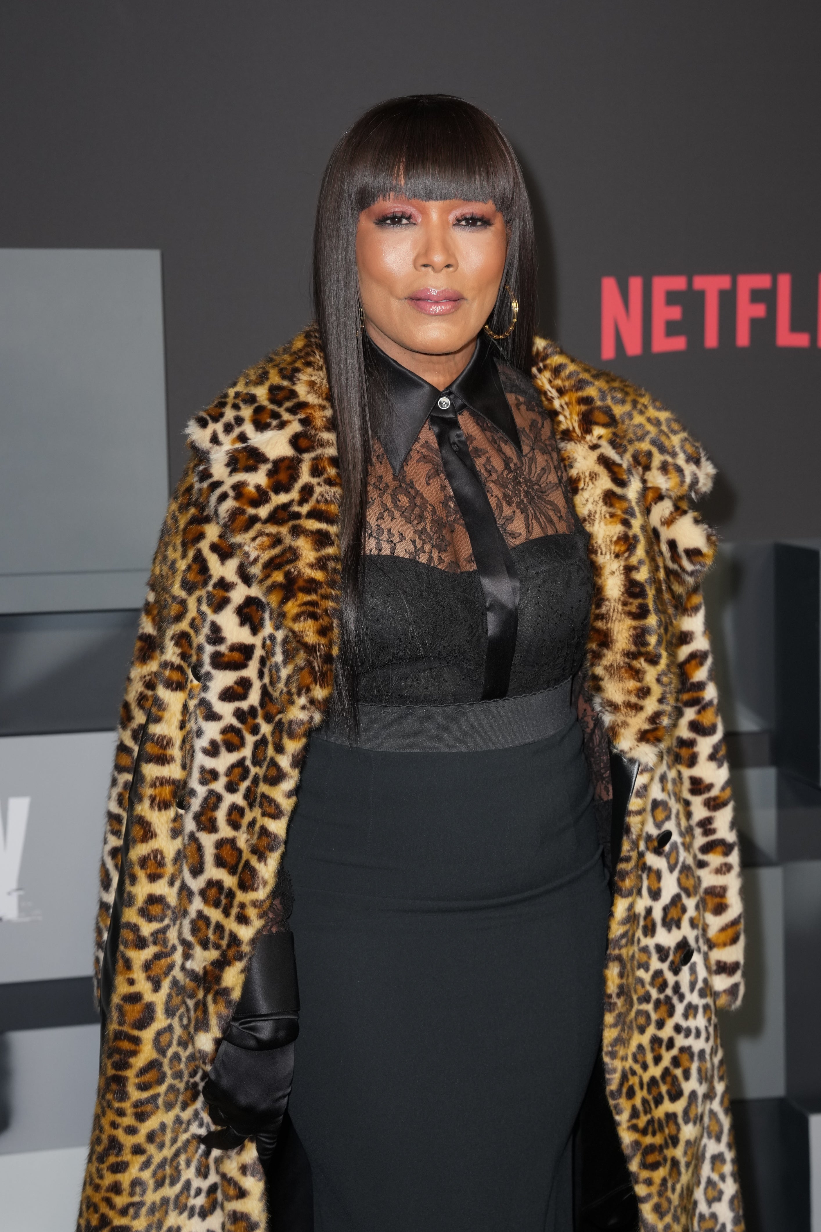Person in leopard print coat, sheer lace top, and high-waisted skirt stands at a Netflix event