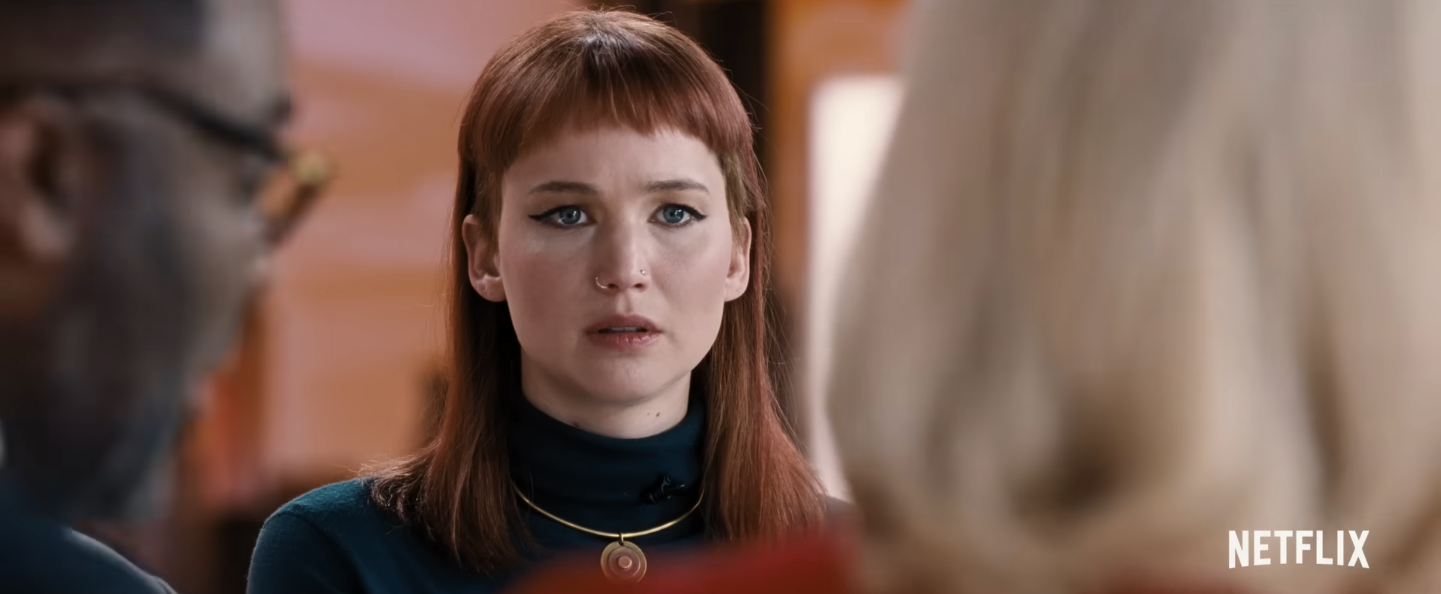 A person with a serious expression is in a conversation with two others. The scene is from a Netflix production