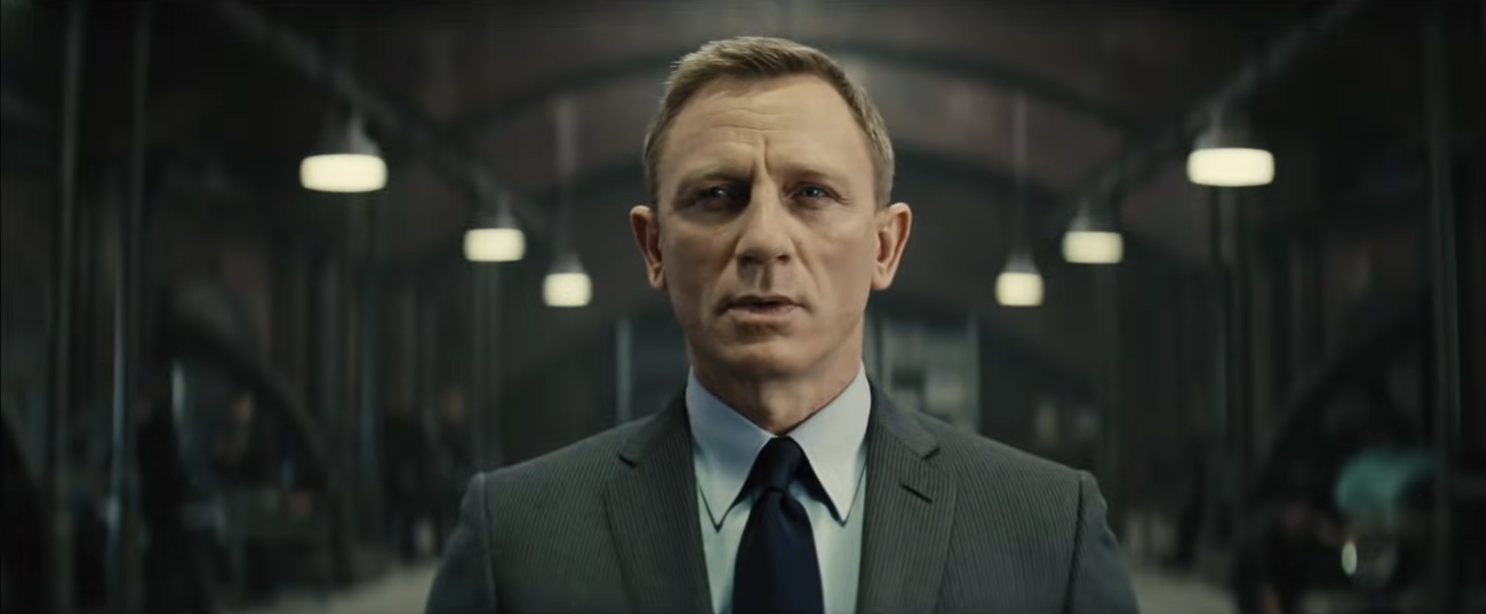 Person in a suit stands in an industrial setting, appearing focused and serious