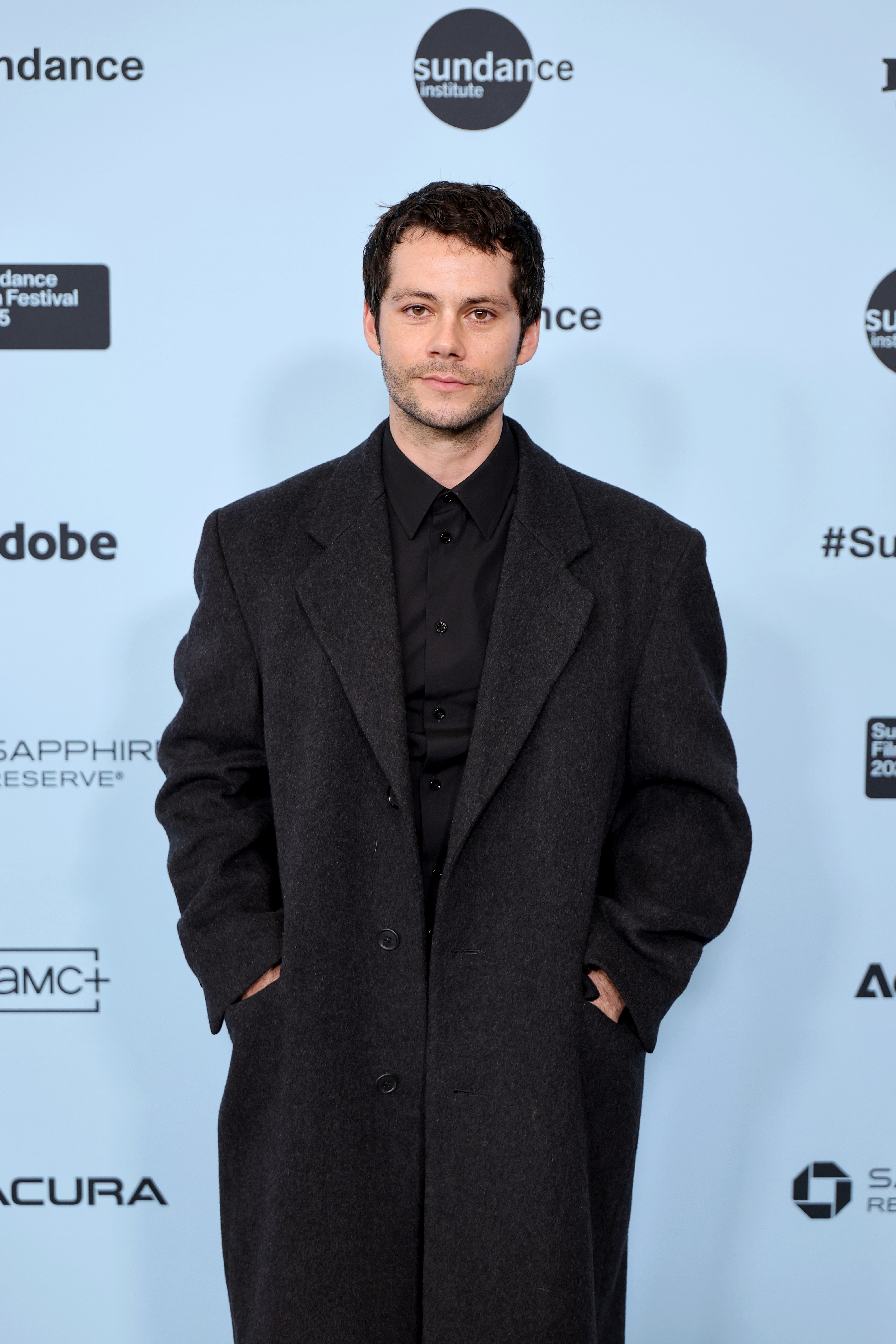 Person in a long, dark coat standing at a Sundance Film Festival event backdrop