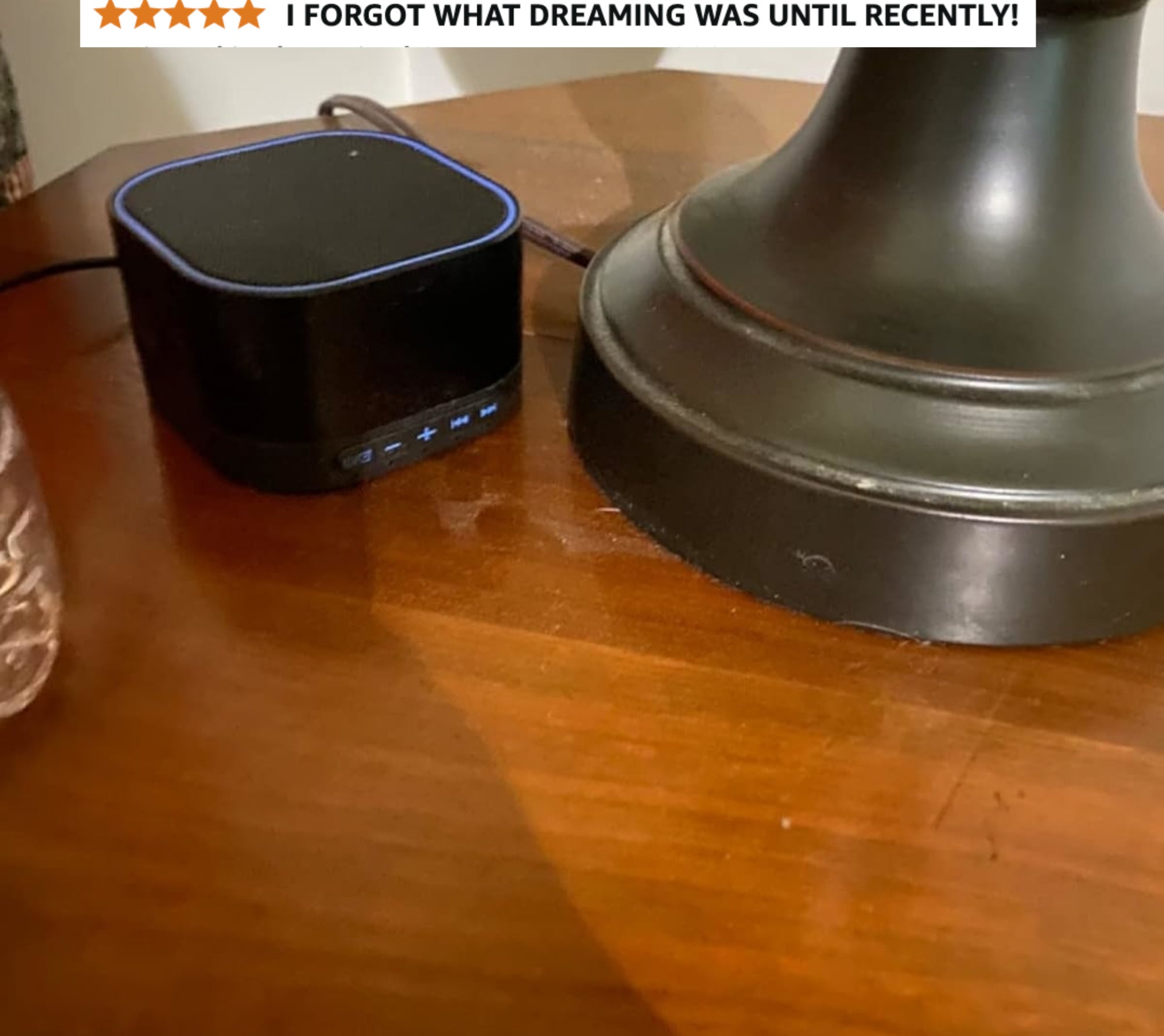 Compact black Bluetooth speaker with blue light edge, placed on a wooden table beside a lamp