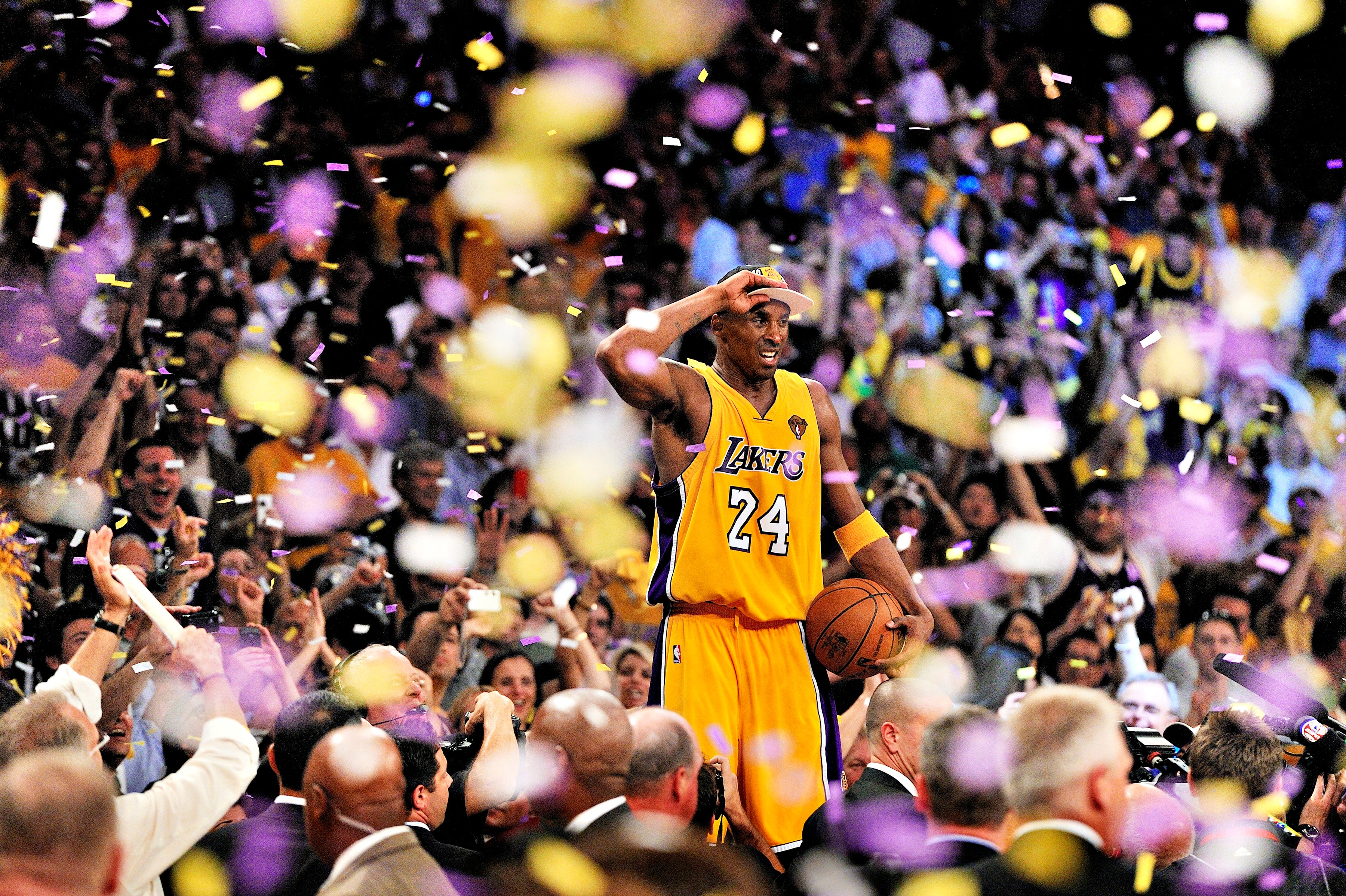 Basketball player in jersey celebrates on court with confetti falling, surrounded by cheering crowd