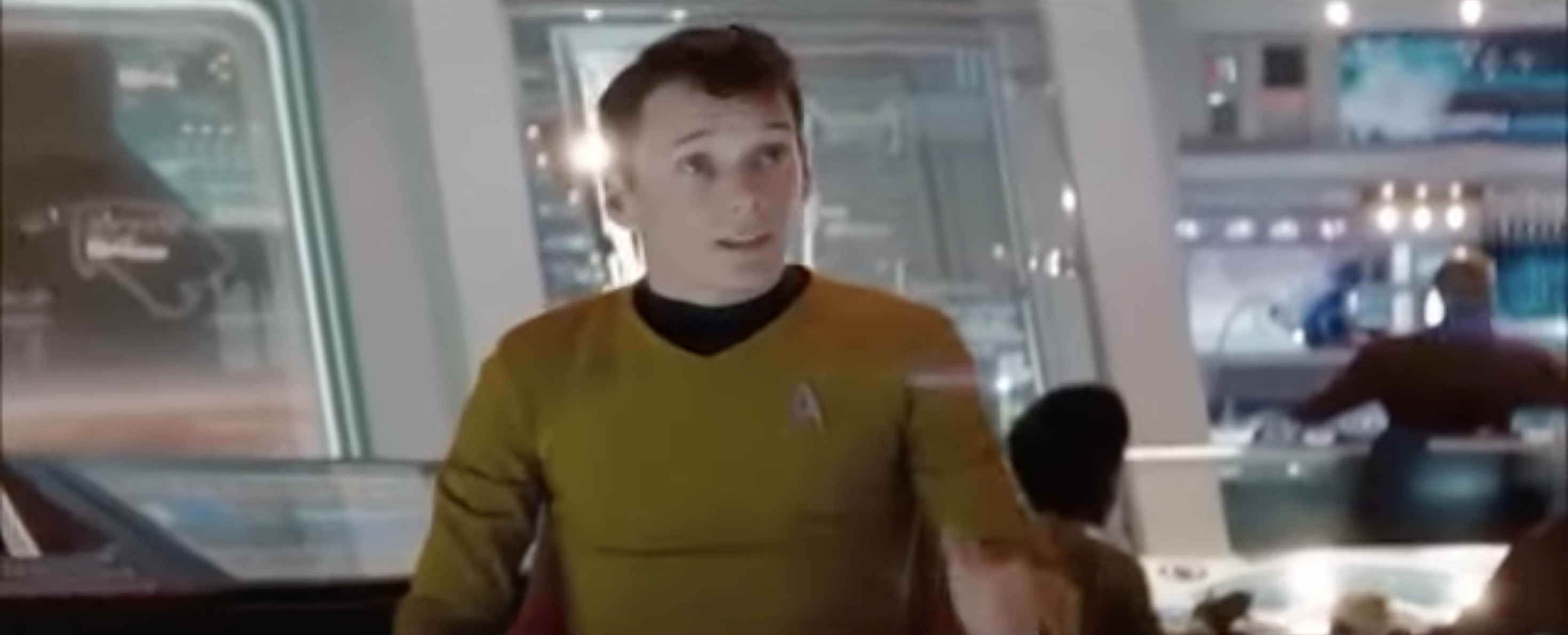 Person in a futuristic spacecraft bridge wearing a sci-fi uniform with a pointed insignia, speaking animatedly
