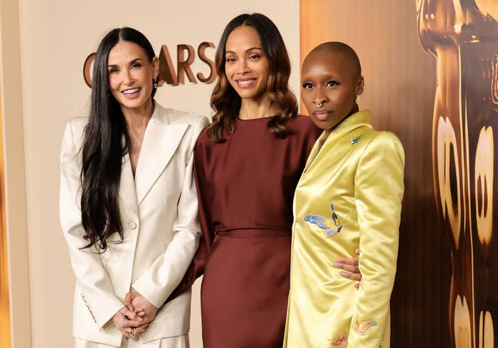 Three individuals in stylish red carpet attire pose together at an event