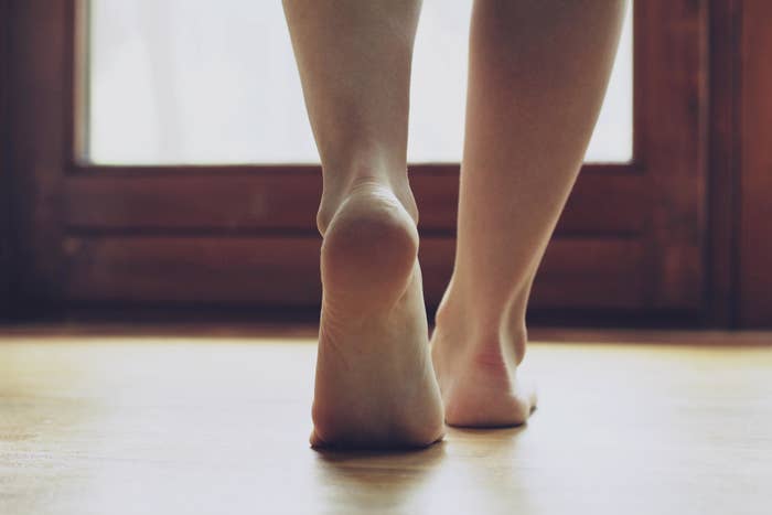 Bare feet walking on a wooden floor towards a window, softly lit by natural light, creating a peaceful atmosphere