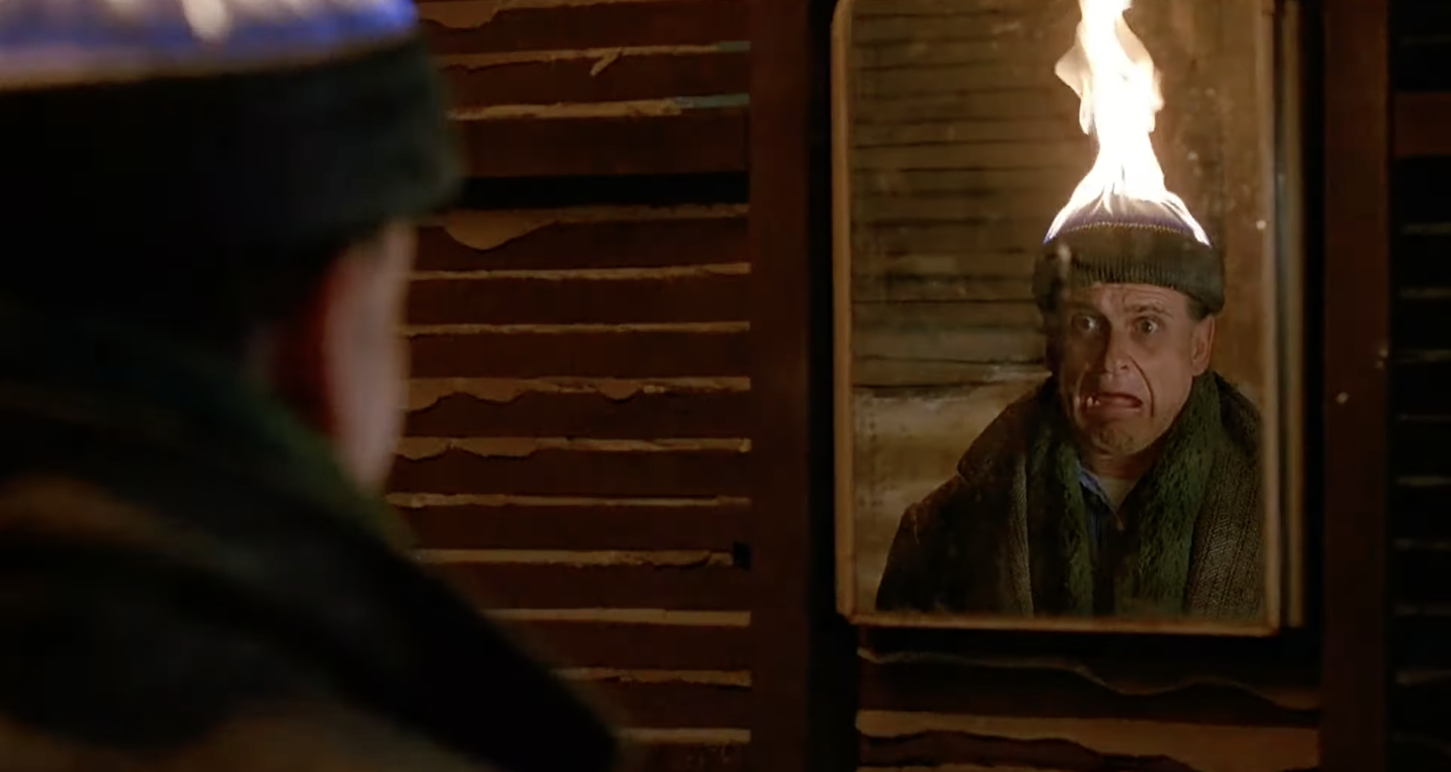 Person in wool hat, staring into a mirror, with the hat comically on fire, conveying shock and surprise. Scene evokes humorous misadventure