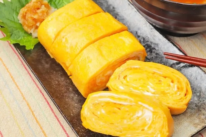 日本のだし巻き卵が皿にのり、味噌汁が隣にある。食欲をそそる盛り付け。