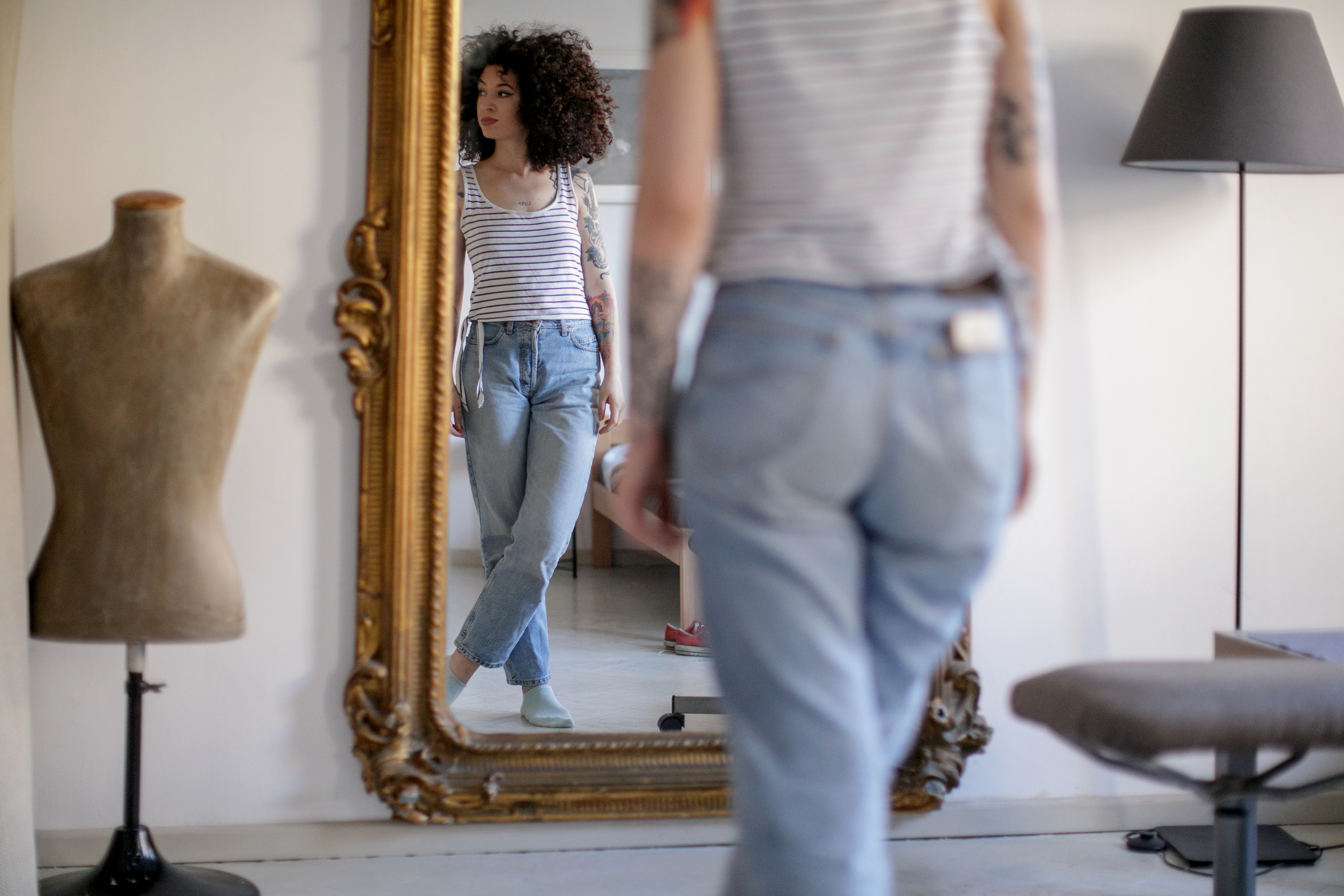 Person i uformell stripete skjorte og jeans ser på refleksjon i utsmykket speil