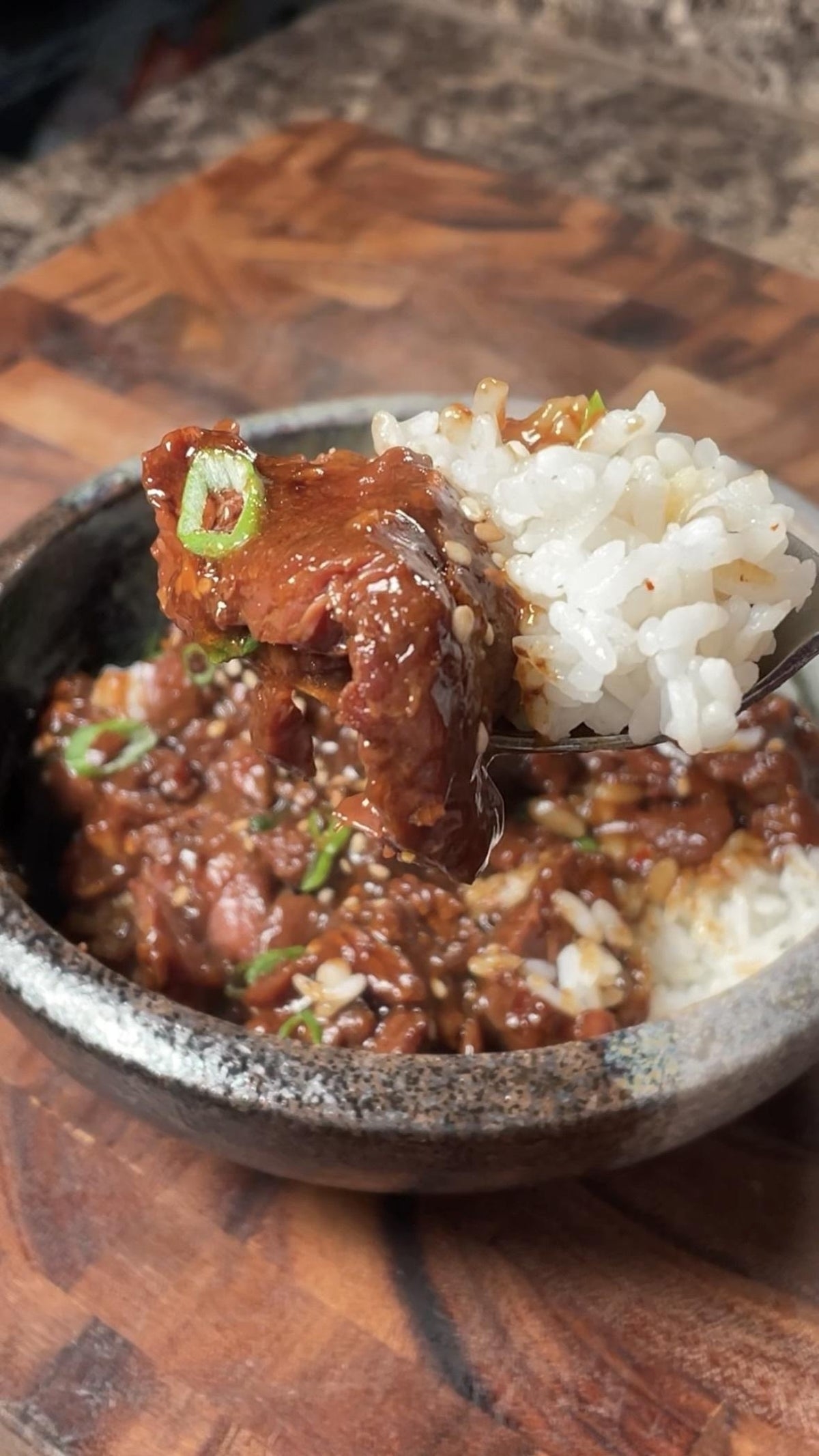 A bowl of rice topped with glazed beef and green onions, with a fork lifting a piece of beef