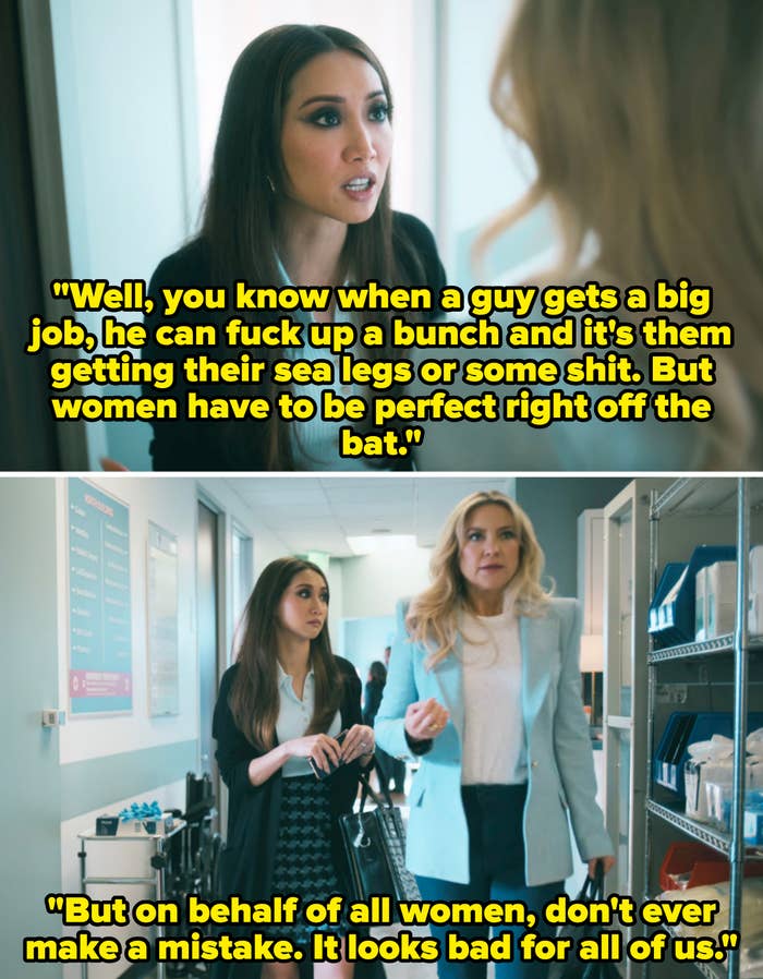 Two women in an office setting, engaged in conversation. One wears a cardigan over a blouse; the other wears a blazer with a skirt