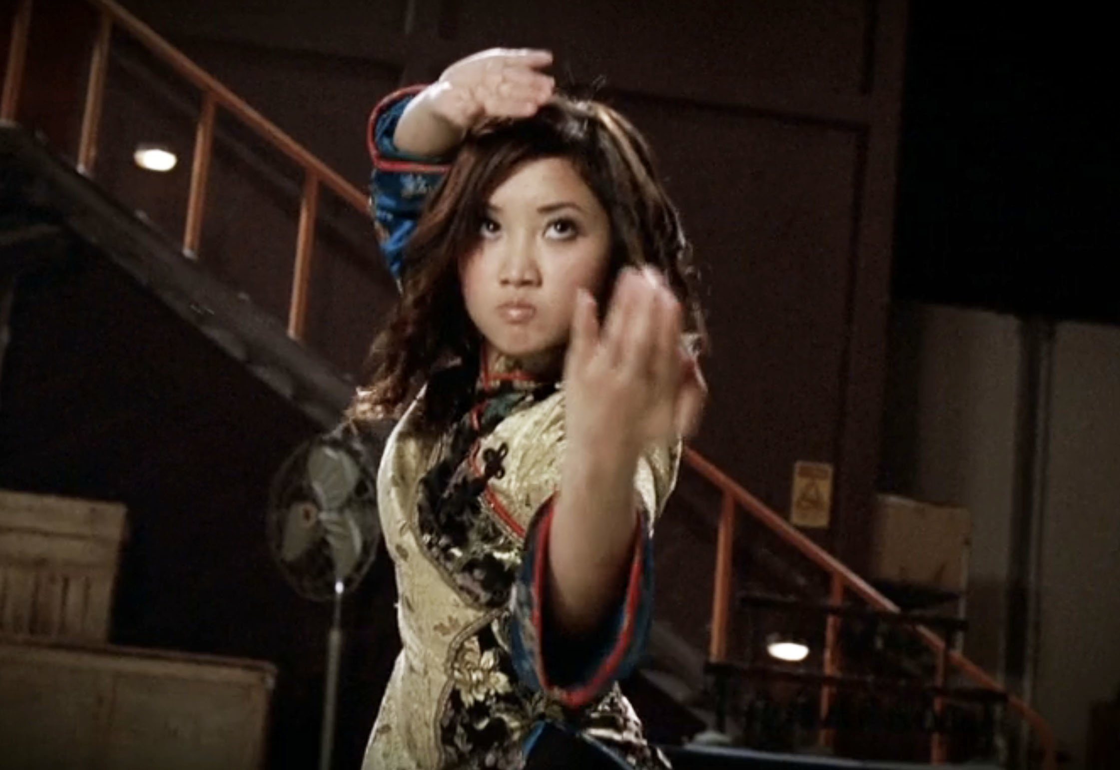 Person in martial arts pose, wearing traditional-inspired attire with ornate patterns, performing in an indoor setting