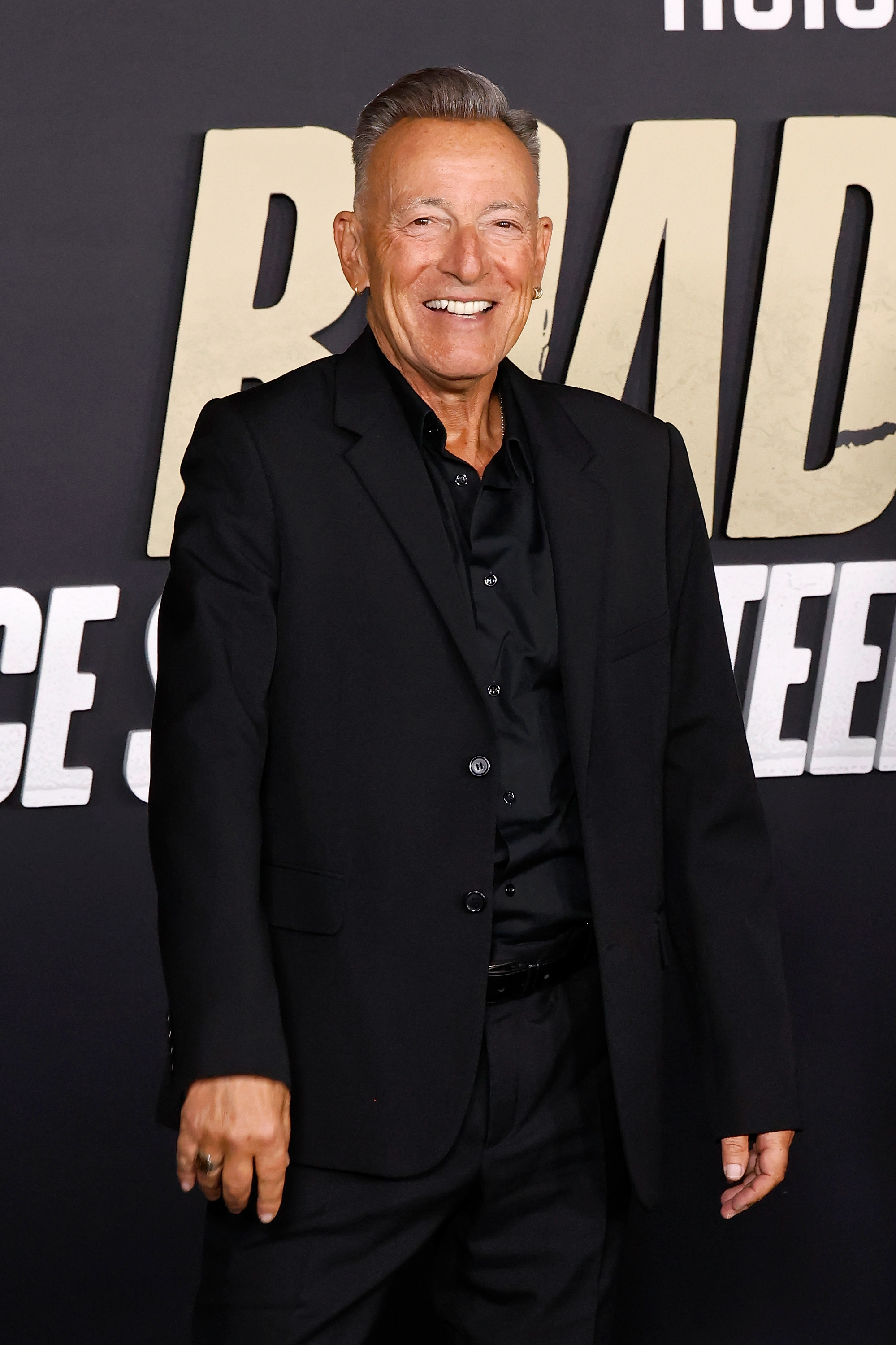 Man successful  a achromatic  suit   smiling connected  a reddish  carpet astatine  an lawsuit   with bold substance   successful  the background