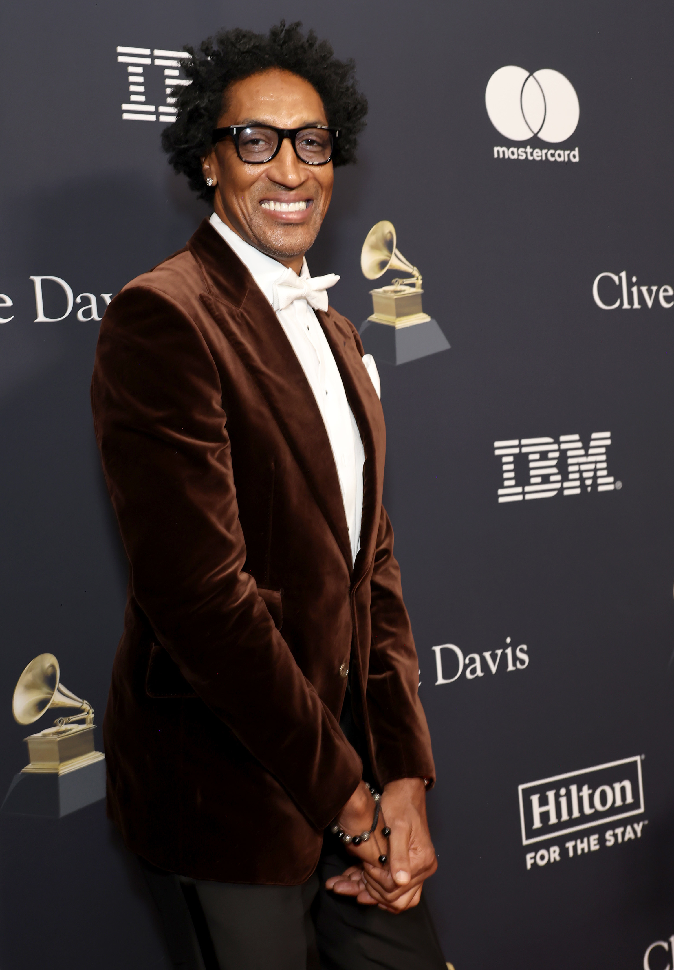 A idiosyncratic   connected  the reddish  carpet wearing a velvet suit   overgarment   and bow tie, posing with a grin  successful  beforehand   of euphony  award-themed logos